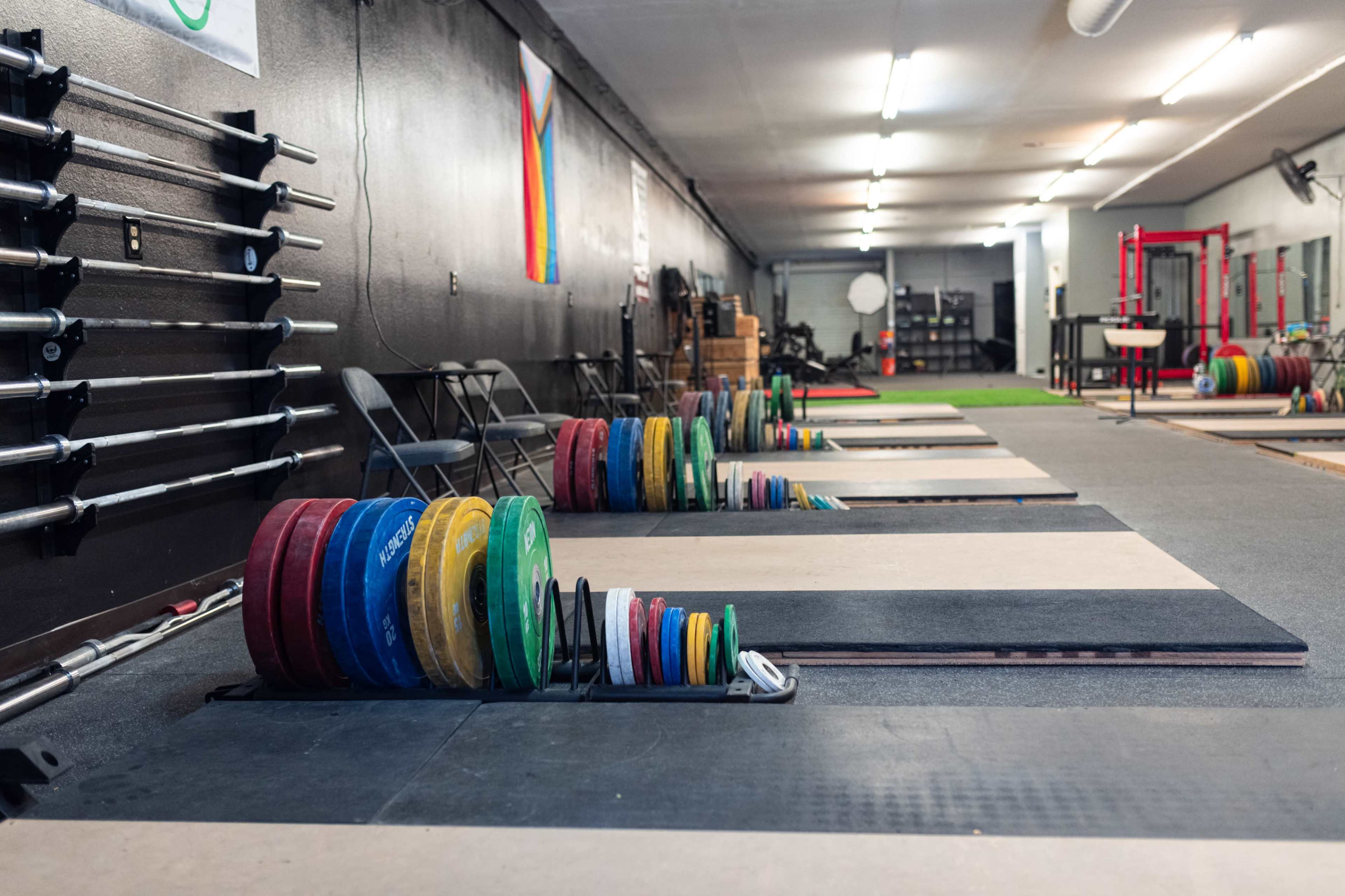 A weightlifting gym with multiple racks of colorful weight plates lined up next to several lifting platforms.