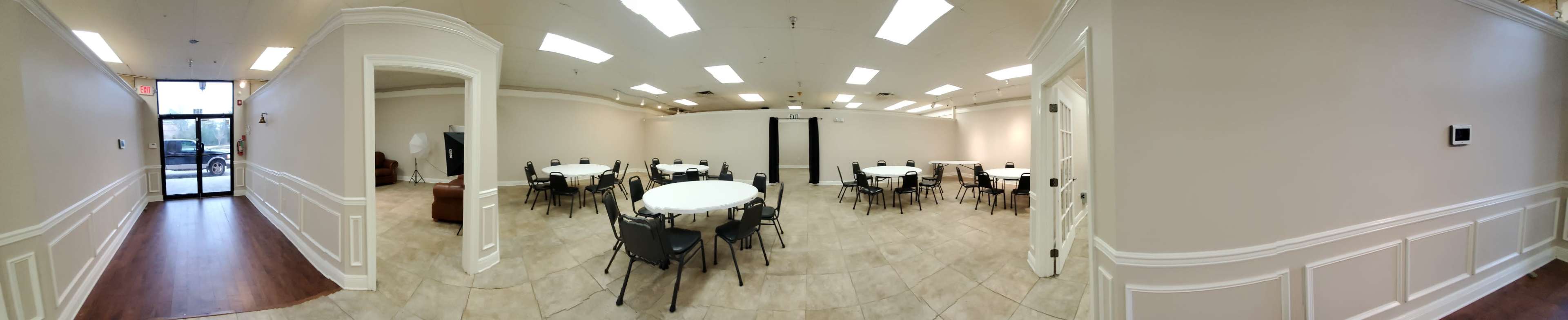 A spacious, well-lit meeting room with several round tables surrounded by chairs, and an entrance visible on the left.