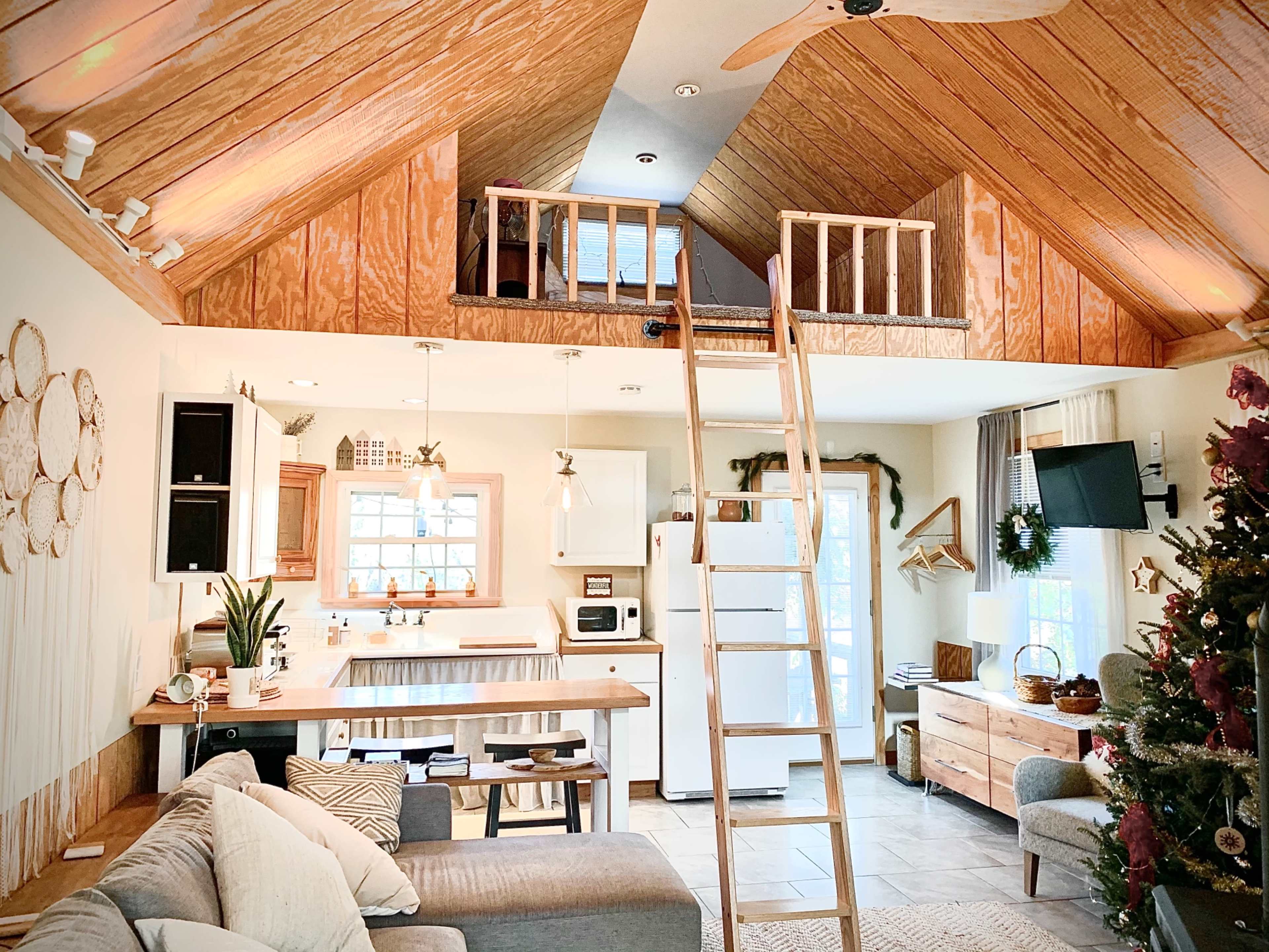 A cozy living space featuring a loft area, wooden beams, a kitchen with a small island, and a staircase leading to the loft.