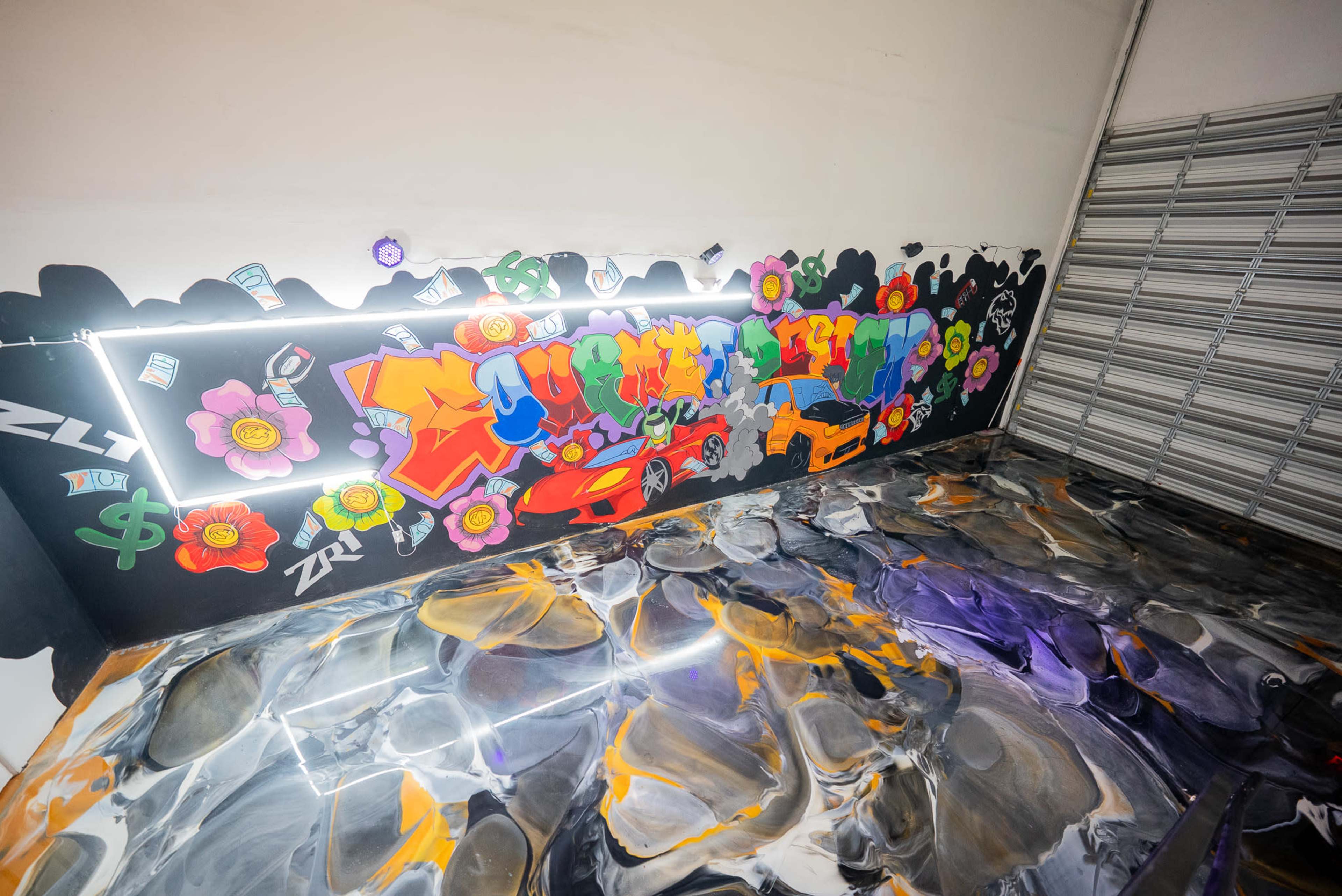 The image shows a graffiti-covered wall with vibrant colors and artistic designs, situated in an indoor space with a reflective, swirled epoxy floor.