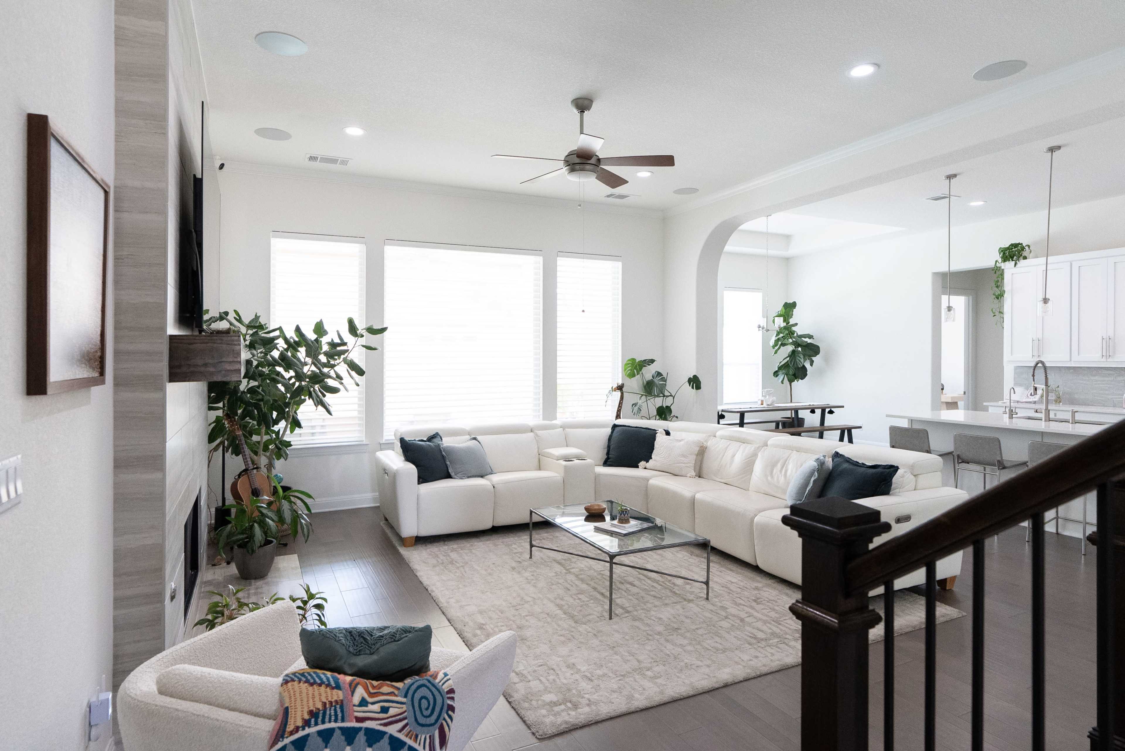 The image shows a modern living room with a white sectional sofa, a coffee table, and large windows that allow natural light to enter the space.