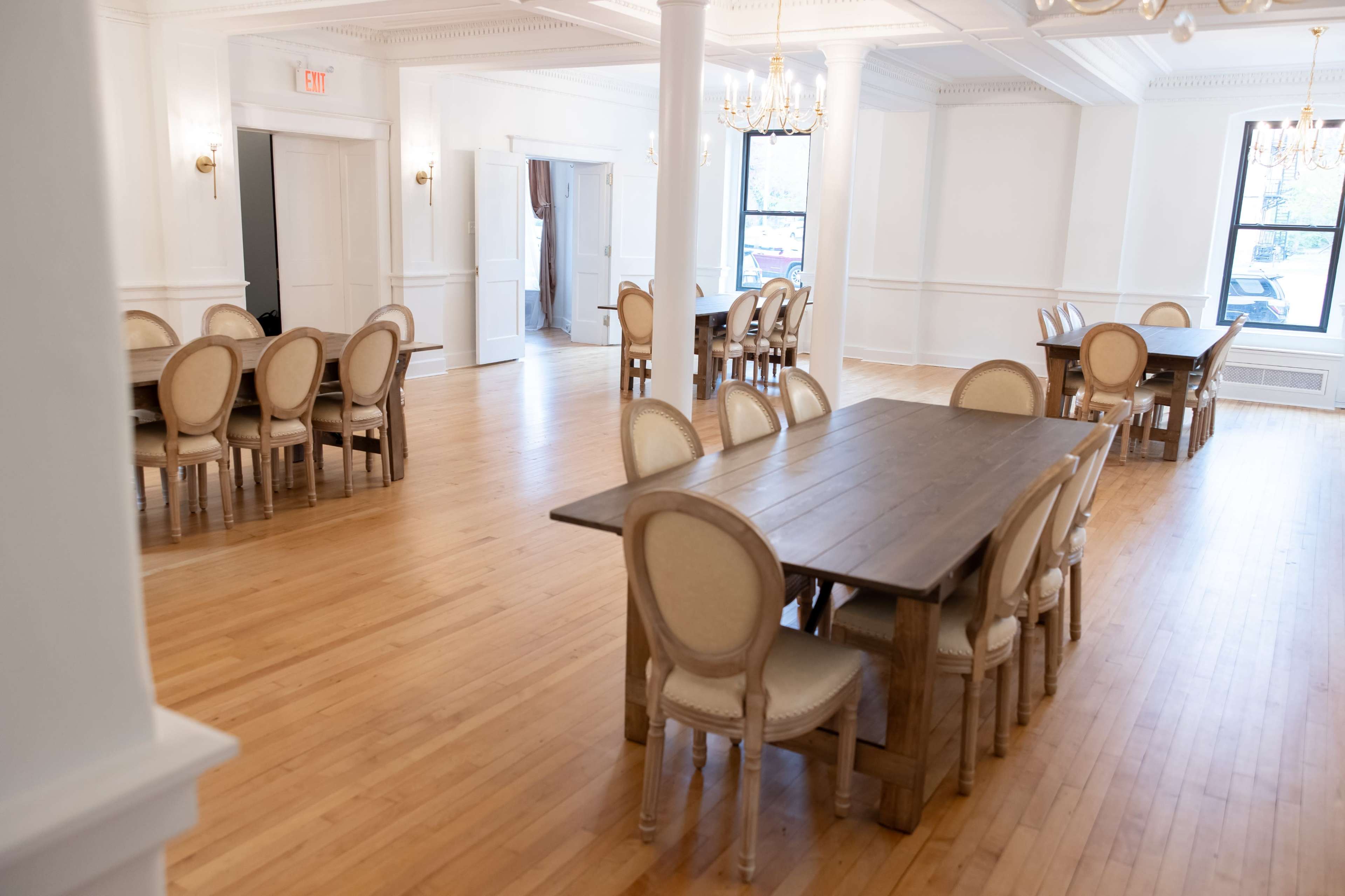 A spacious, well-lit room with wooden floors, featuring several tables and chairs arranged for dining or meetings.