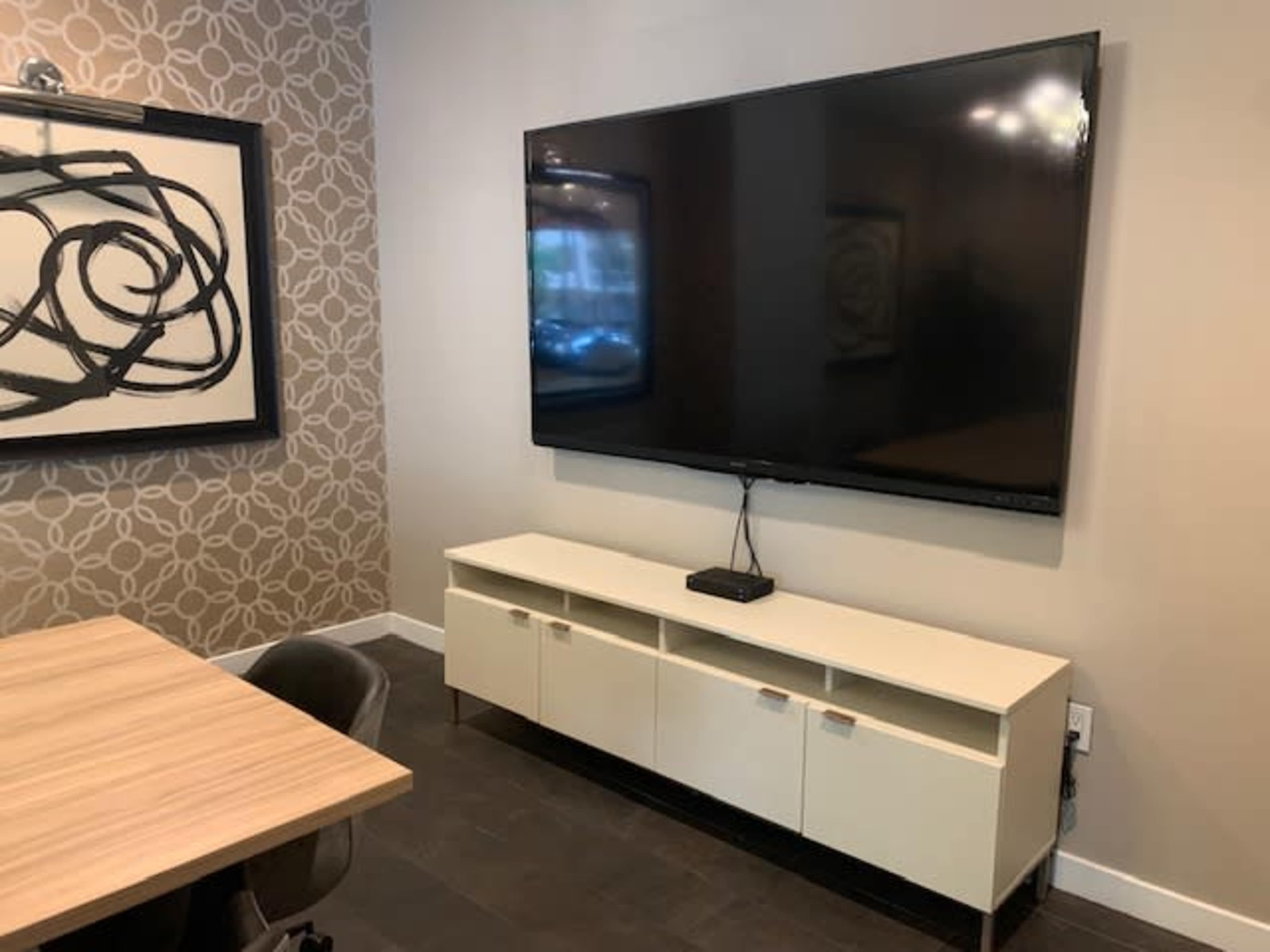 The image shows a modern room with a large flat-screen TV mounted on the wall above a white console with storage compartments.