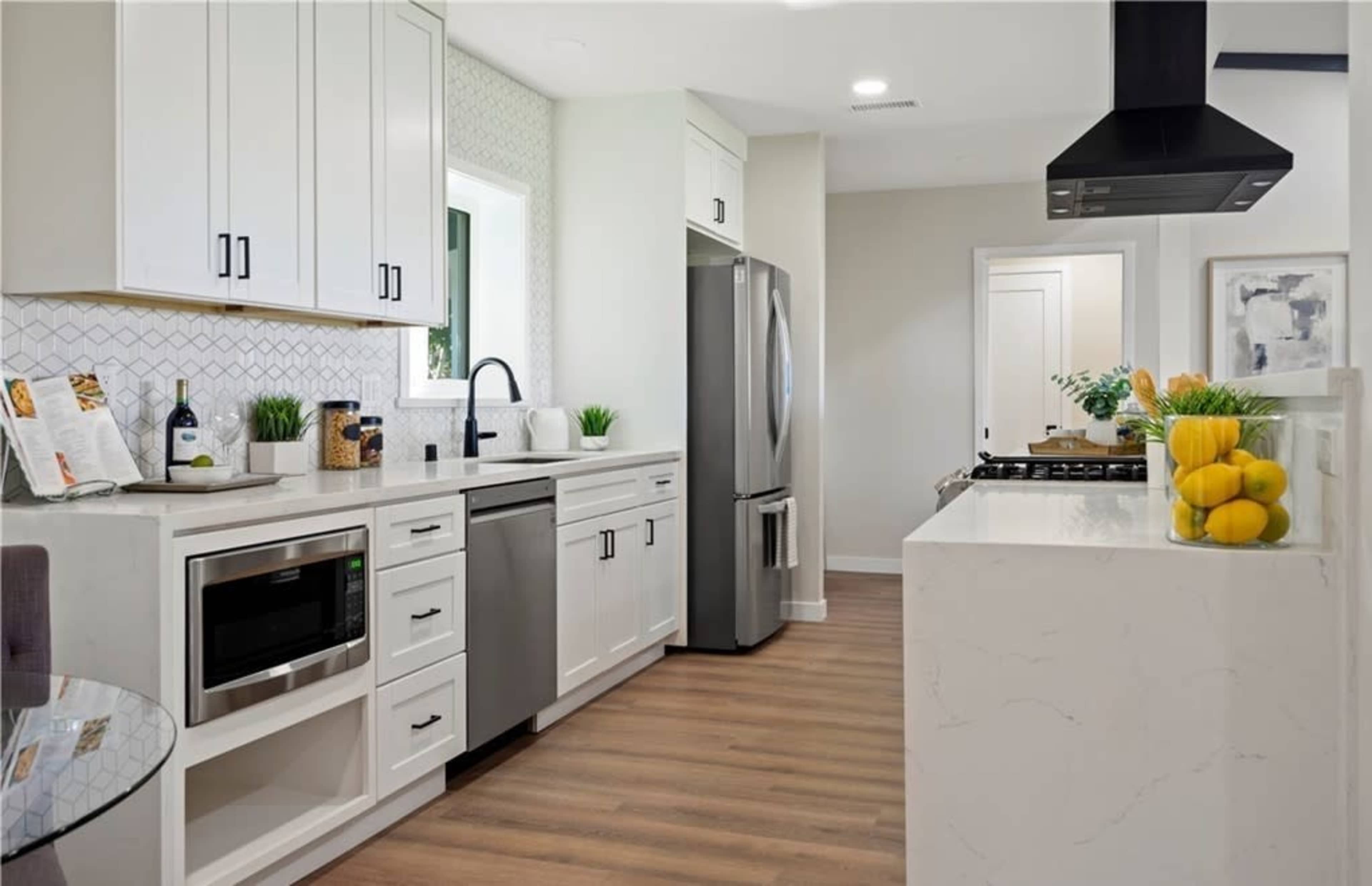 A modern kitchen features white cabinets, stainless steel appliances, and a sleek countertop with a view of a dining area.