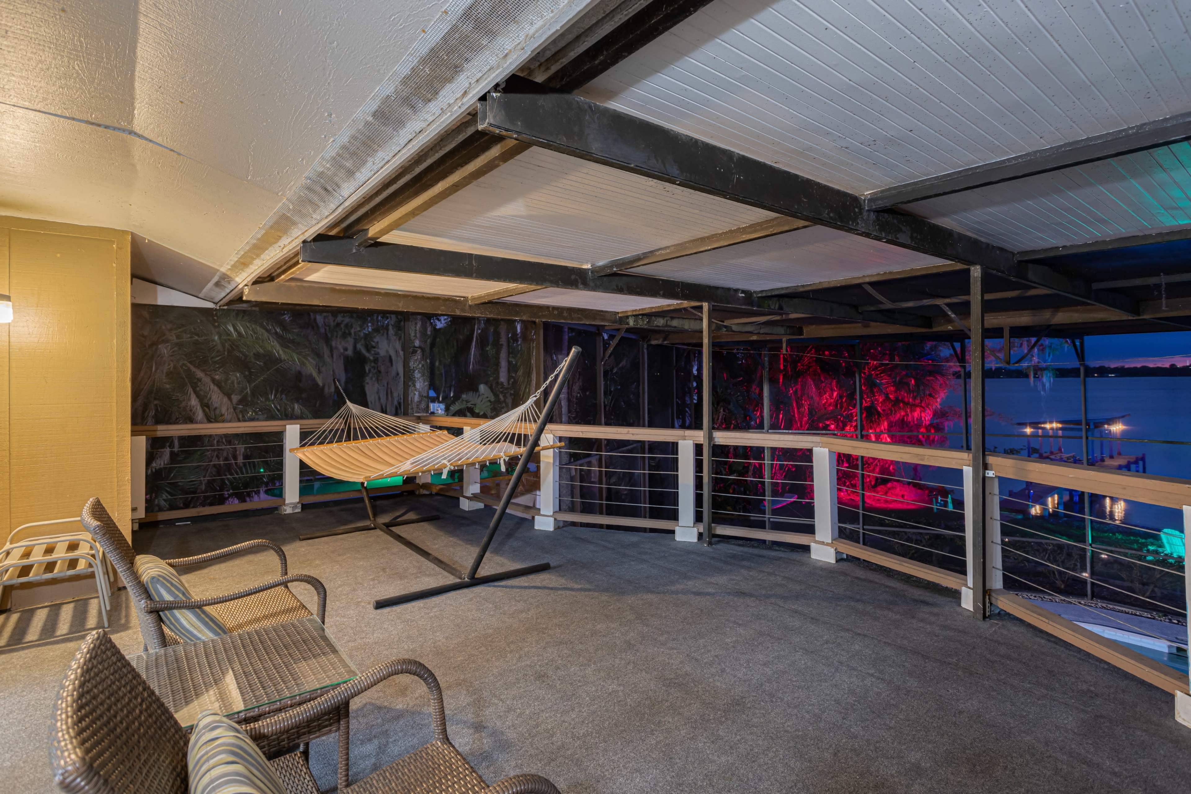 The image shows a spacious covered balcony with a hammock hanging in the center and several chairs arranged around it.