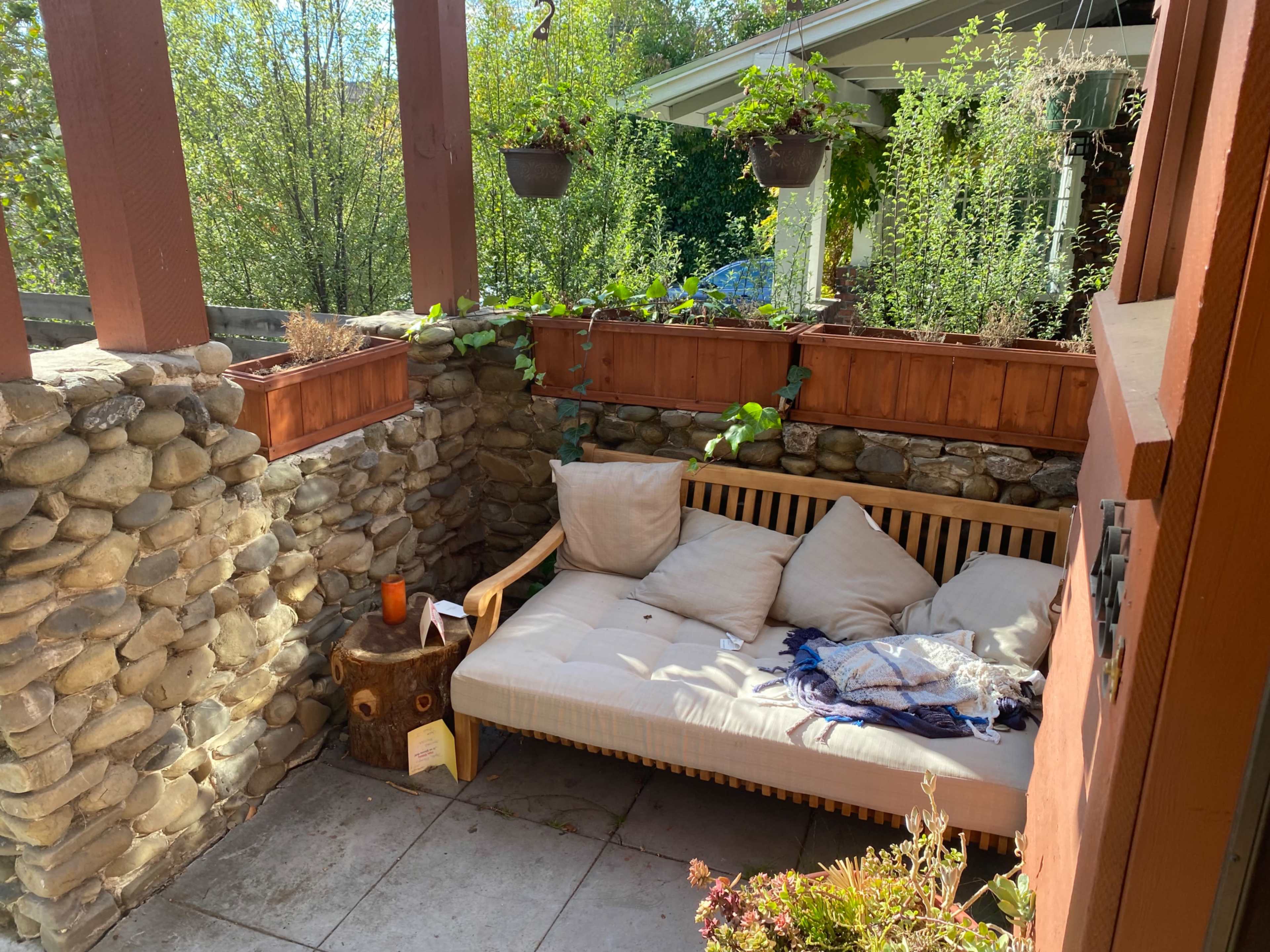 A sheltered outdoor seating area with a wooden couch, stone walls, and potted plants.