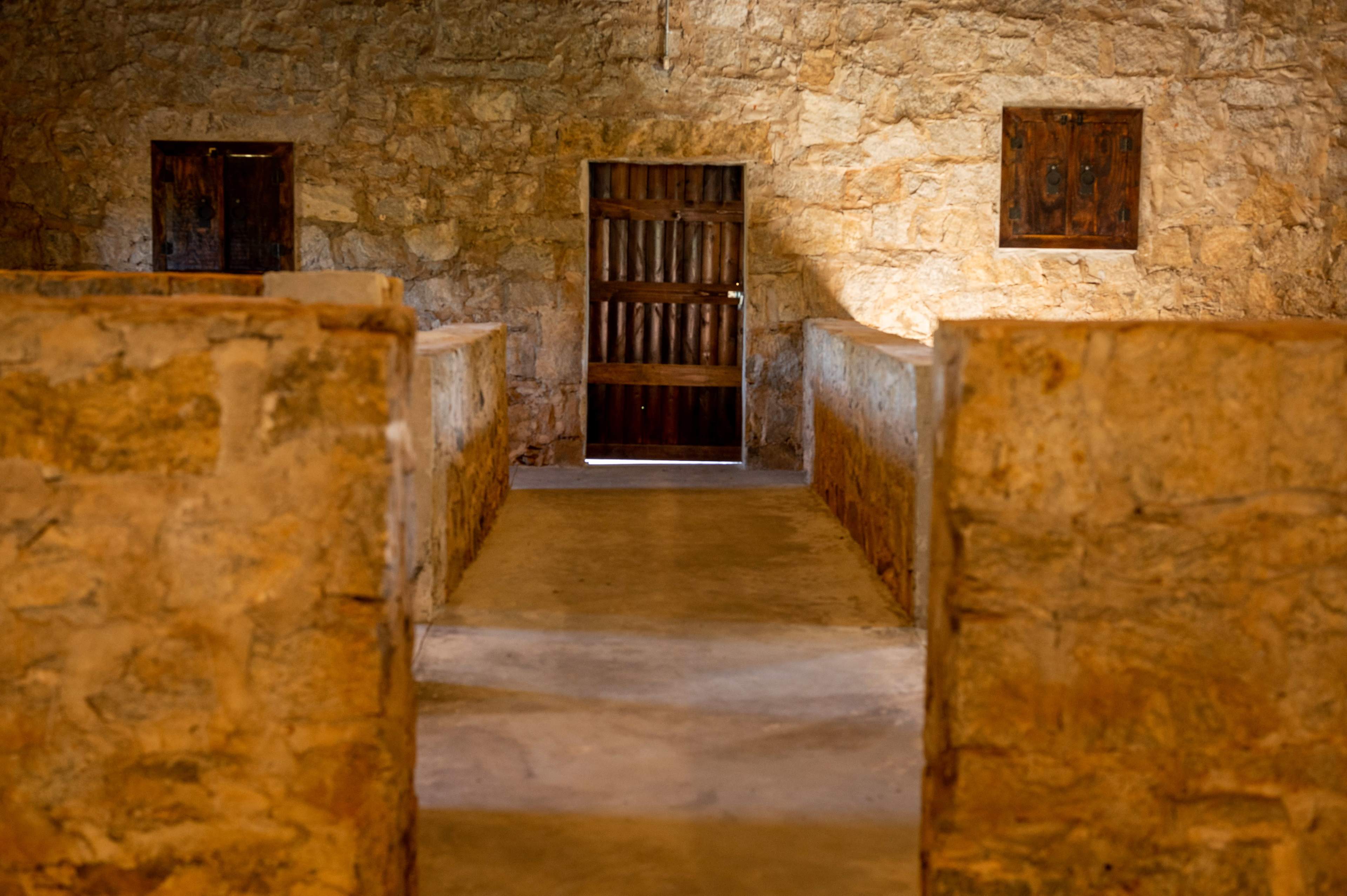 The image shows a stone-walled room with a wooden door at the far end and openings on either side, leading to an empty space.