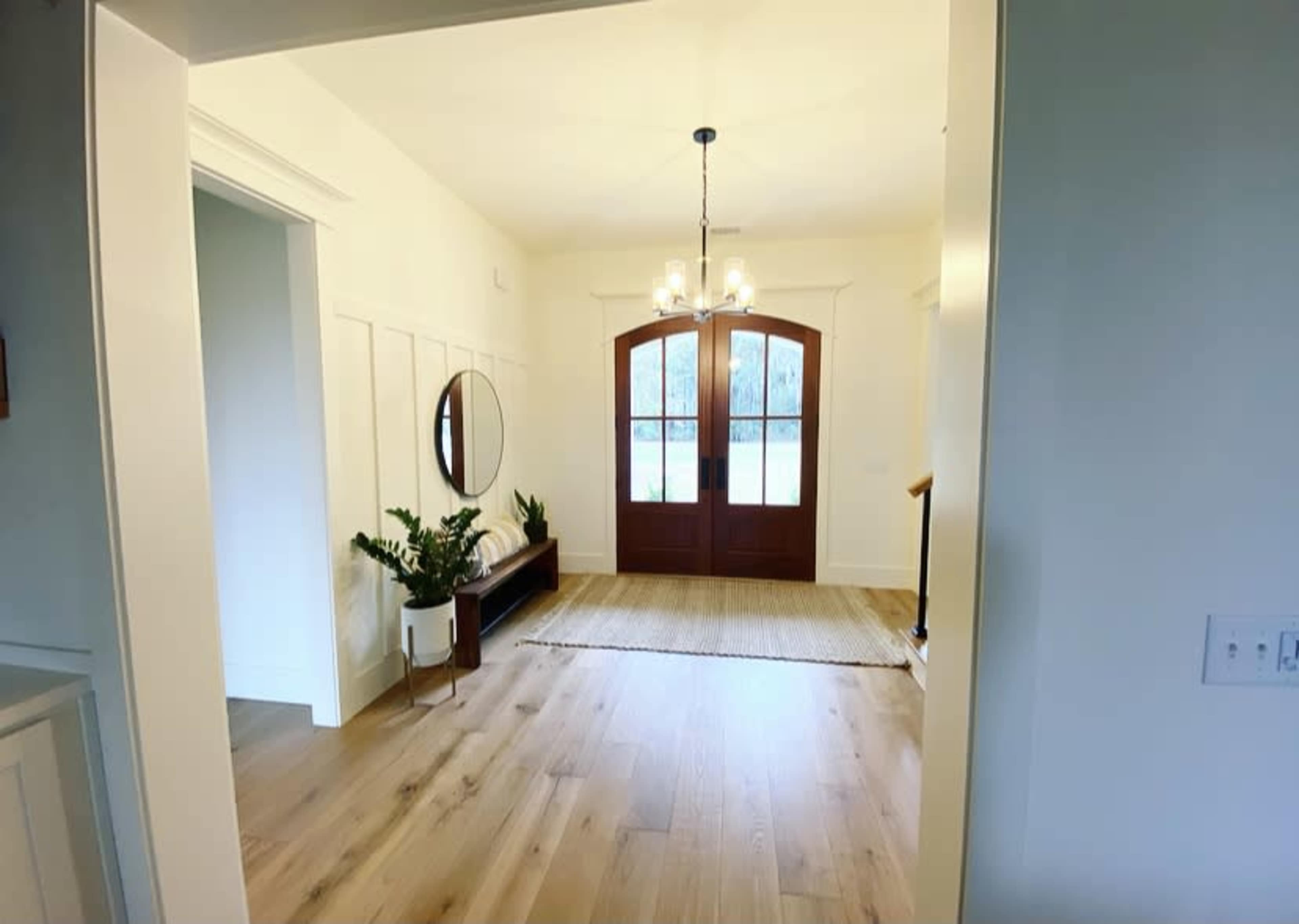 An entryway featuring a pair of double doors, a round mirror on the wall, a console table, and a rug on the wooden floor.