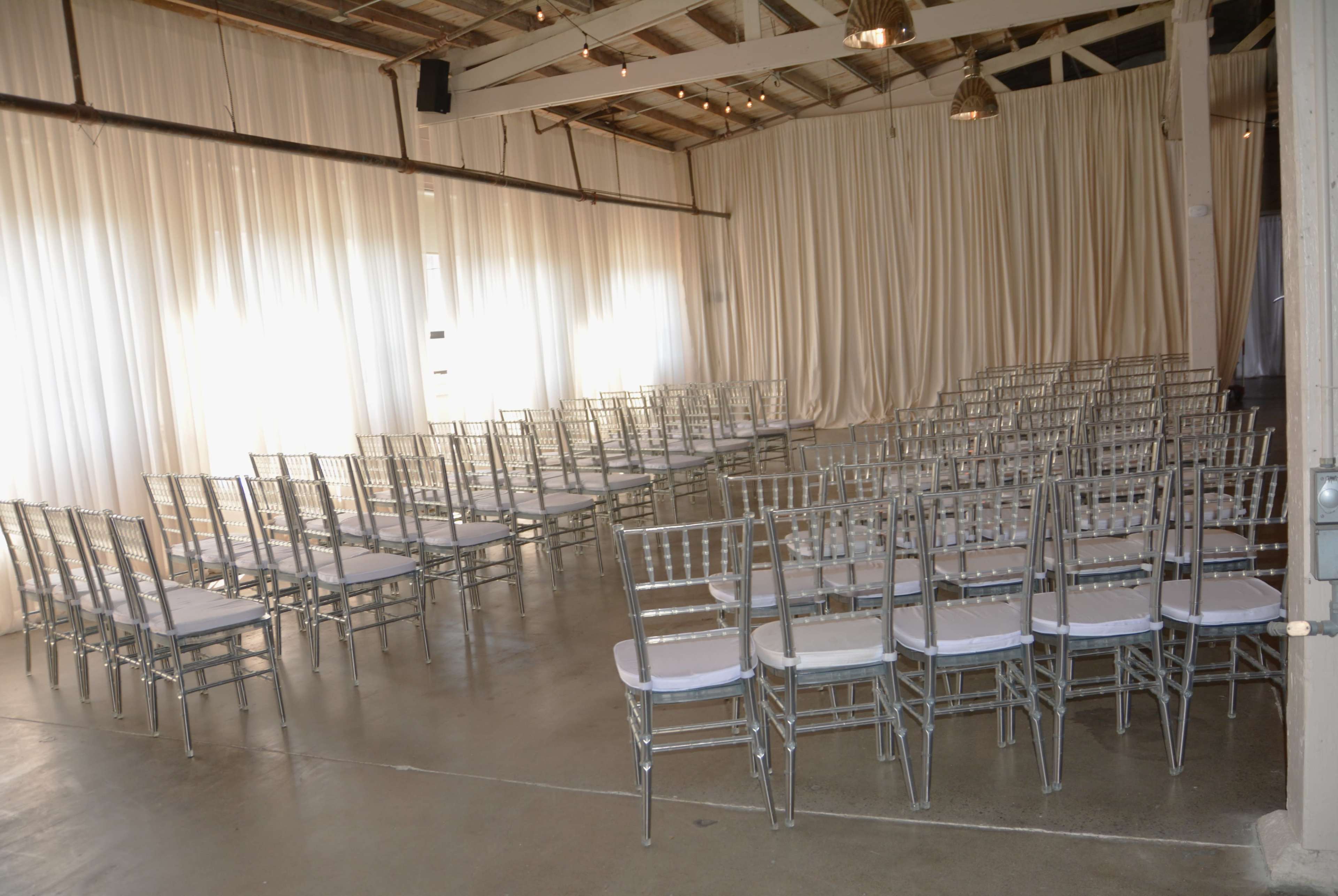 A spacious indoor venue set up with rows of silver chiavari chairs arranged for an event.