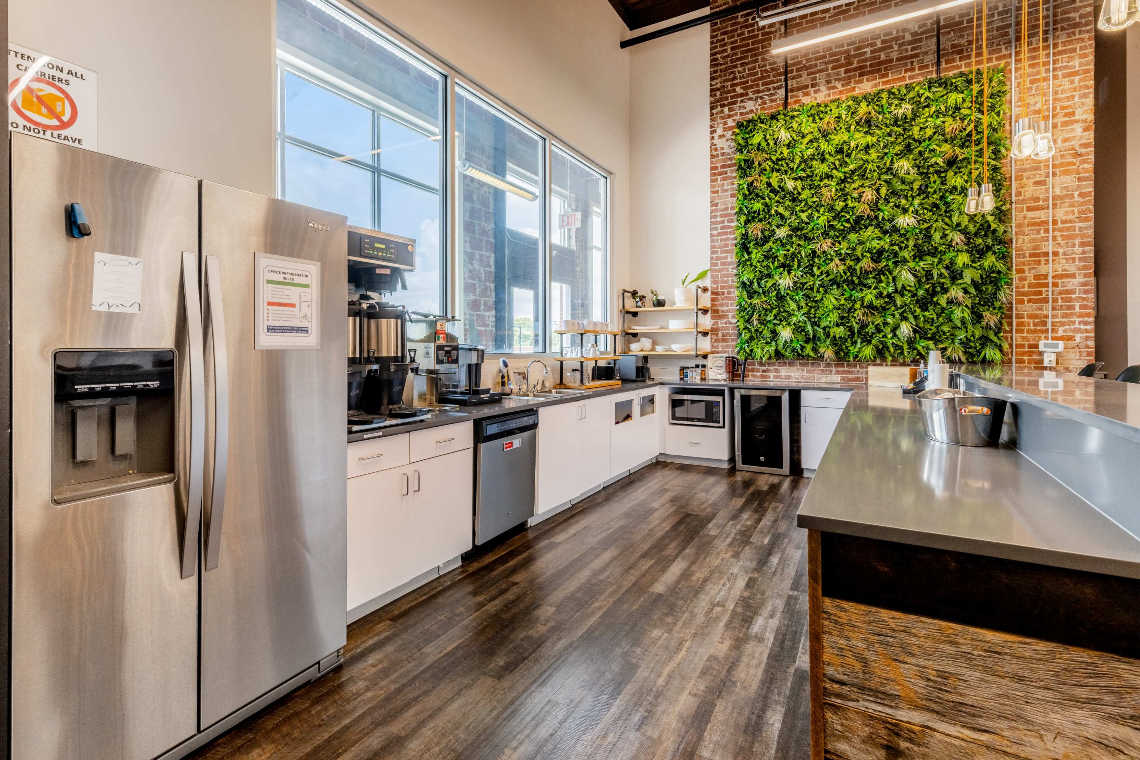 The image shows a modern kitchen area featuring stainless steel appliances, a brick wall with a vertical garden, and a sleek countertop.