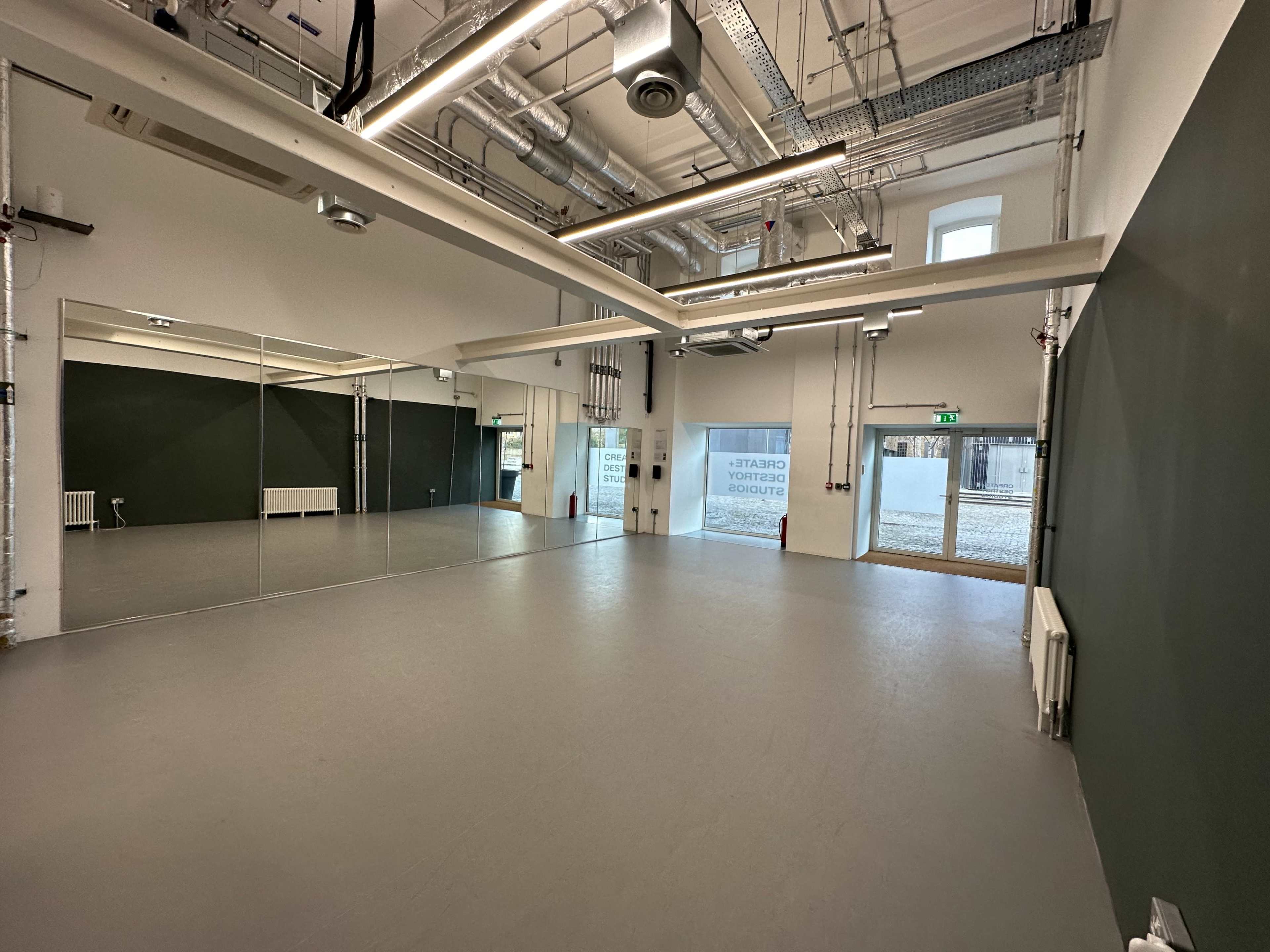 The image shows a spacious, empty room with large mirrors on one wall and a doorway leading outside.