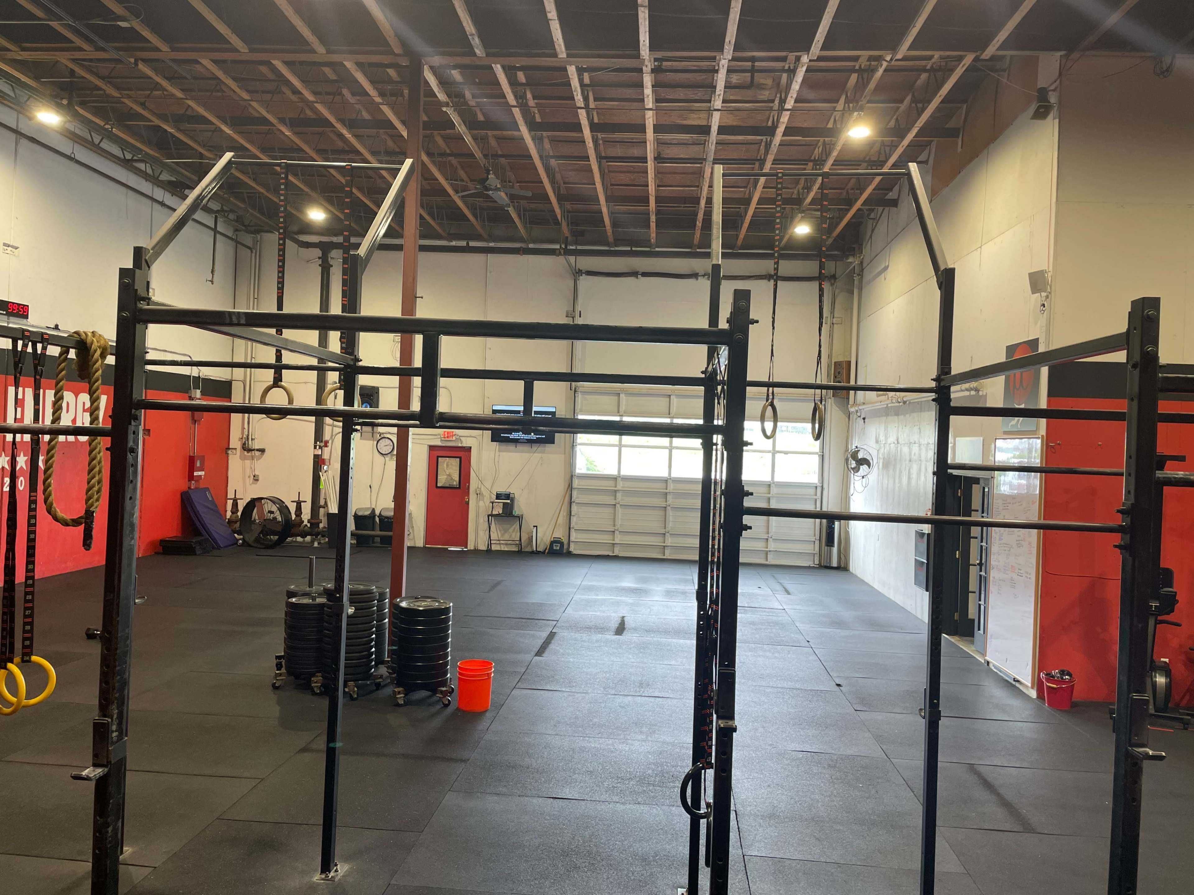 A spacious gym with exercise equipment, including pull-up bars and weight plates, against red and white walls.