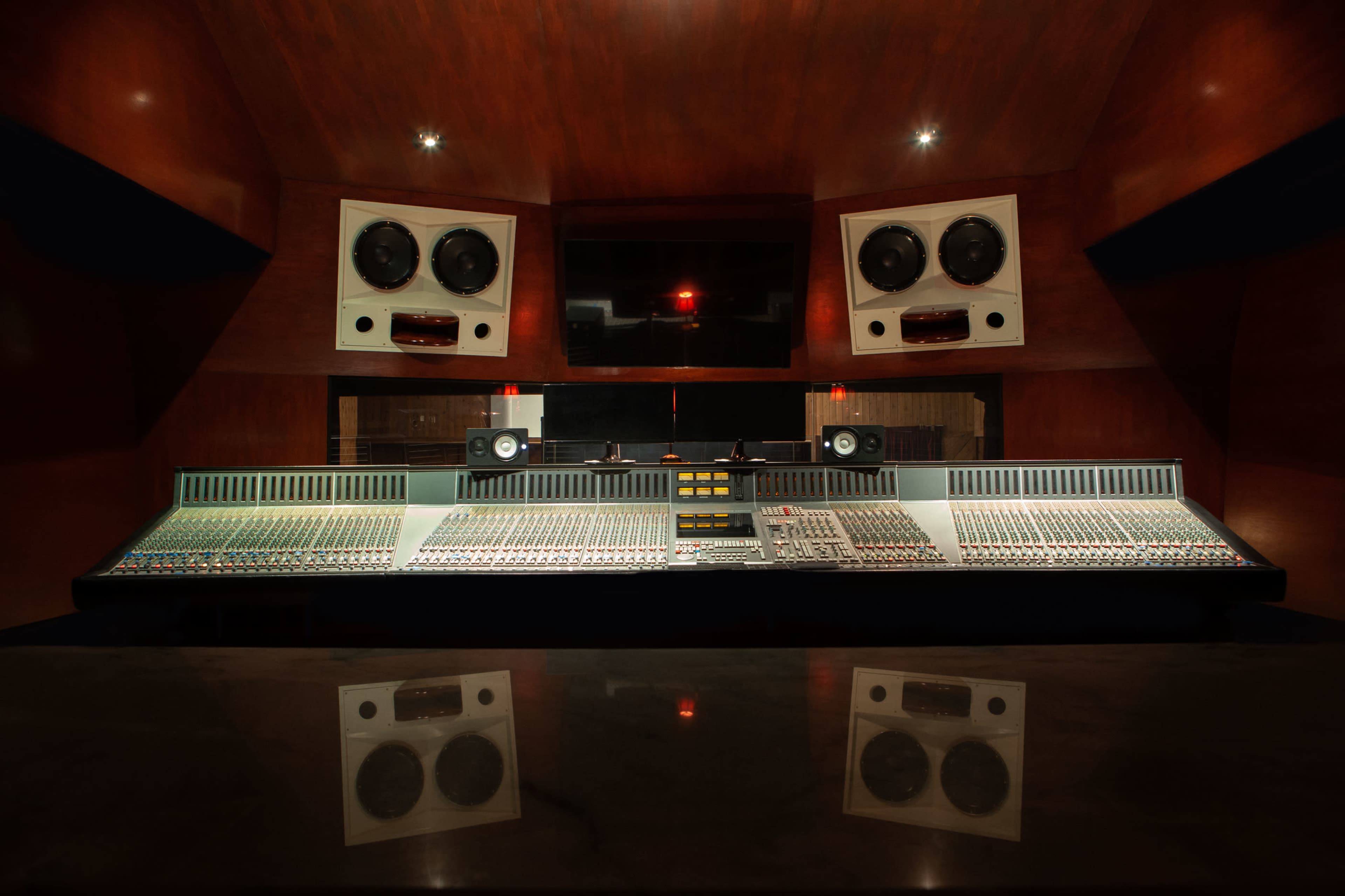 A sound recording studio with a large mixing console, prominent speakers, and a wood-paneled interior.
