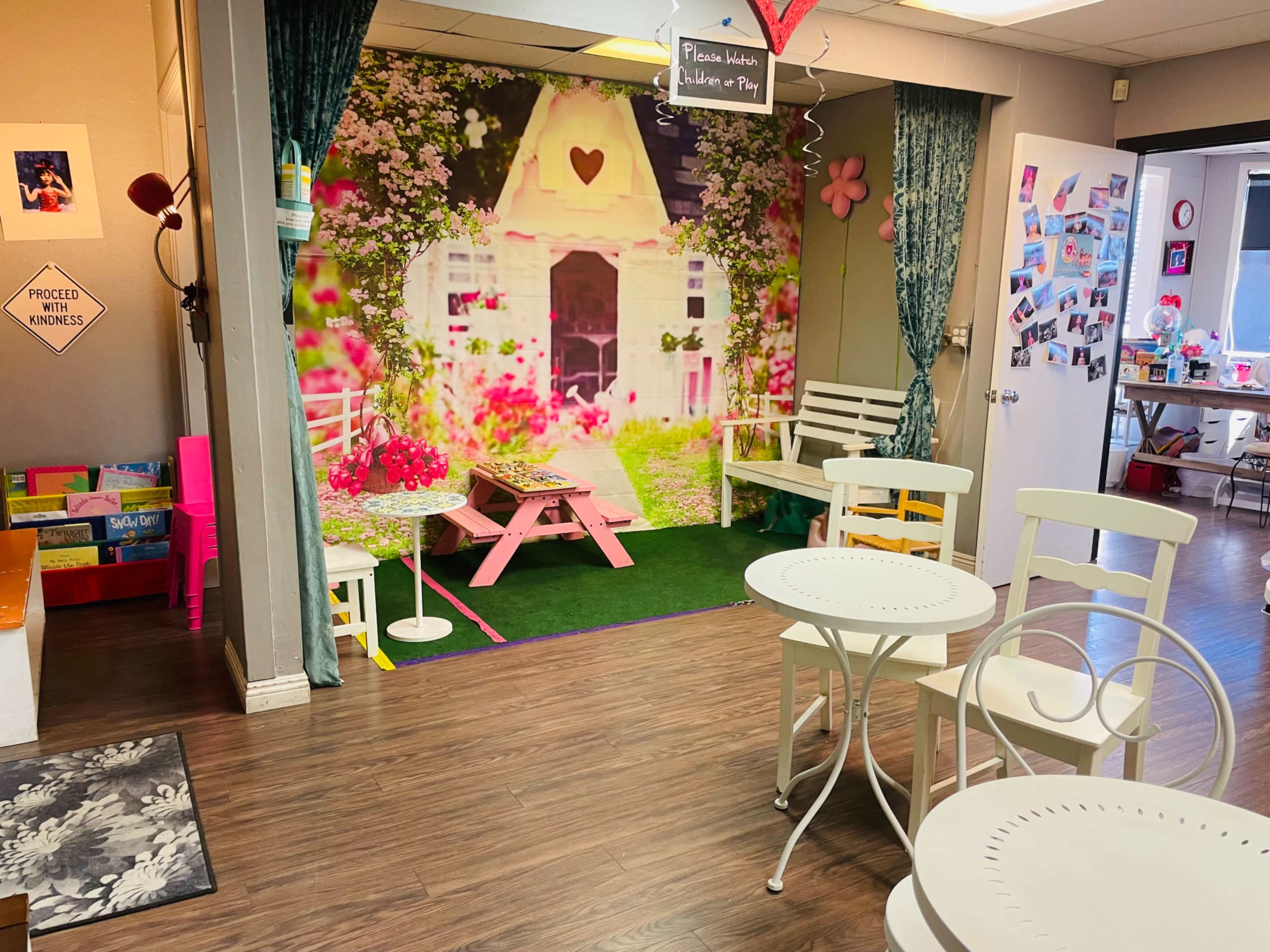 A small, decorative room with pastel-colored chairs and a vibrant backdrop featuring a charming cottage surrounded by flowers.