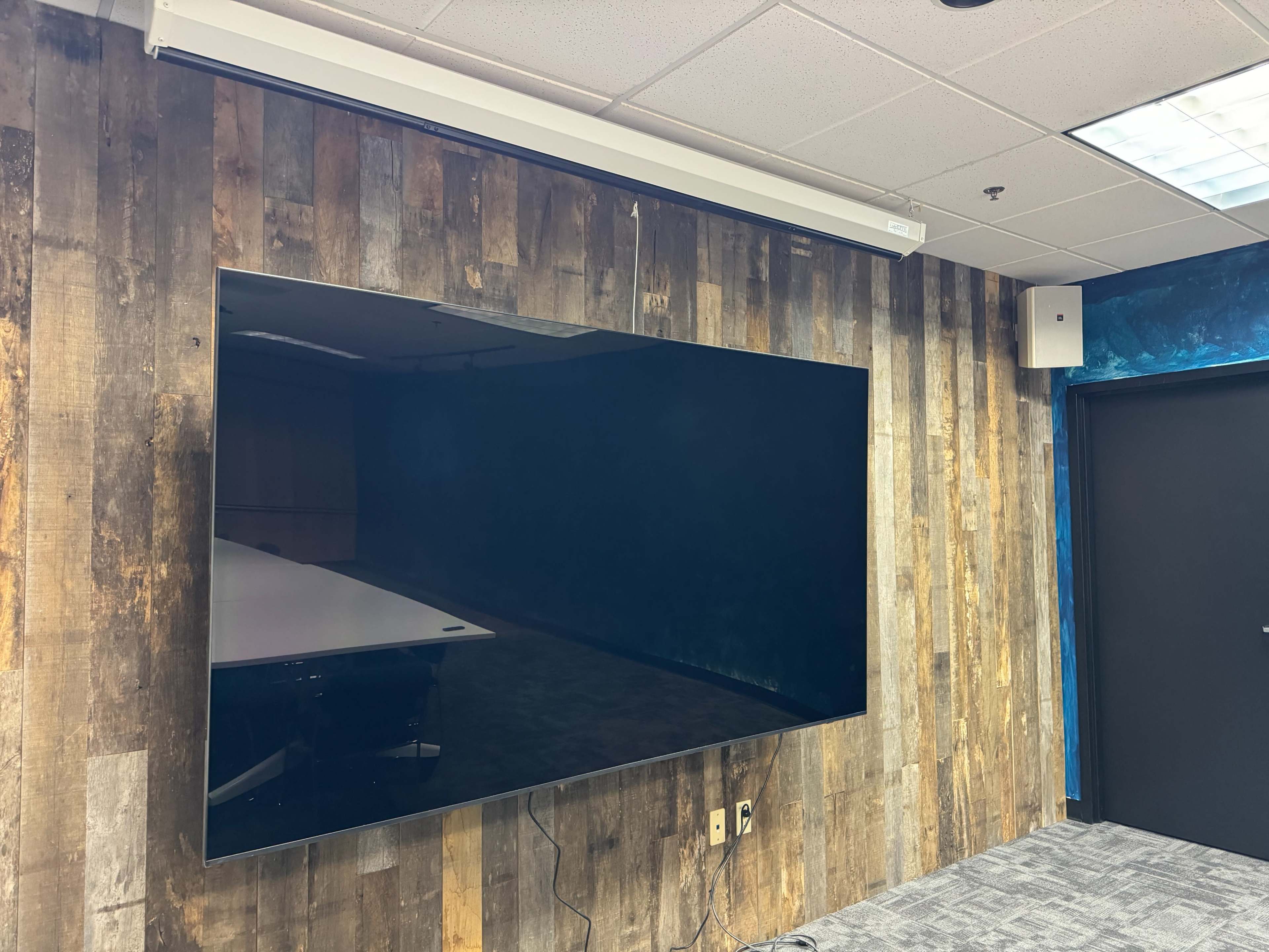 A large flat-screen television is mounted on a wooden-paneled wall in an office setting.