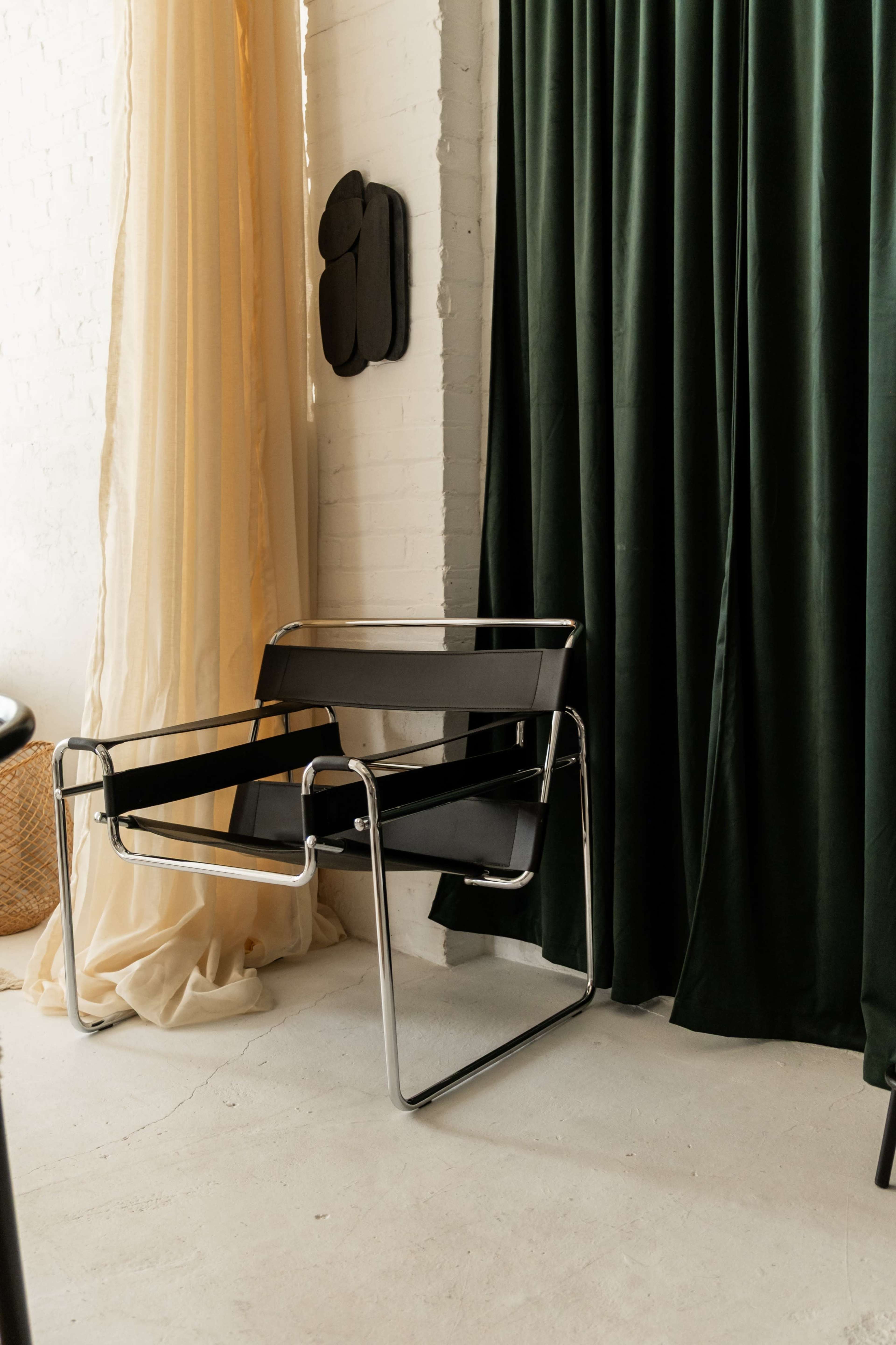 A sleek, modern chair with a metal frame and black fabric sits beside flowing curtains in shades of yellow and green.