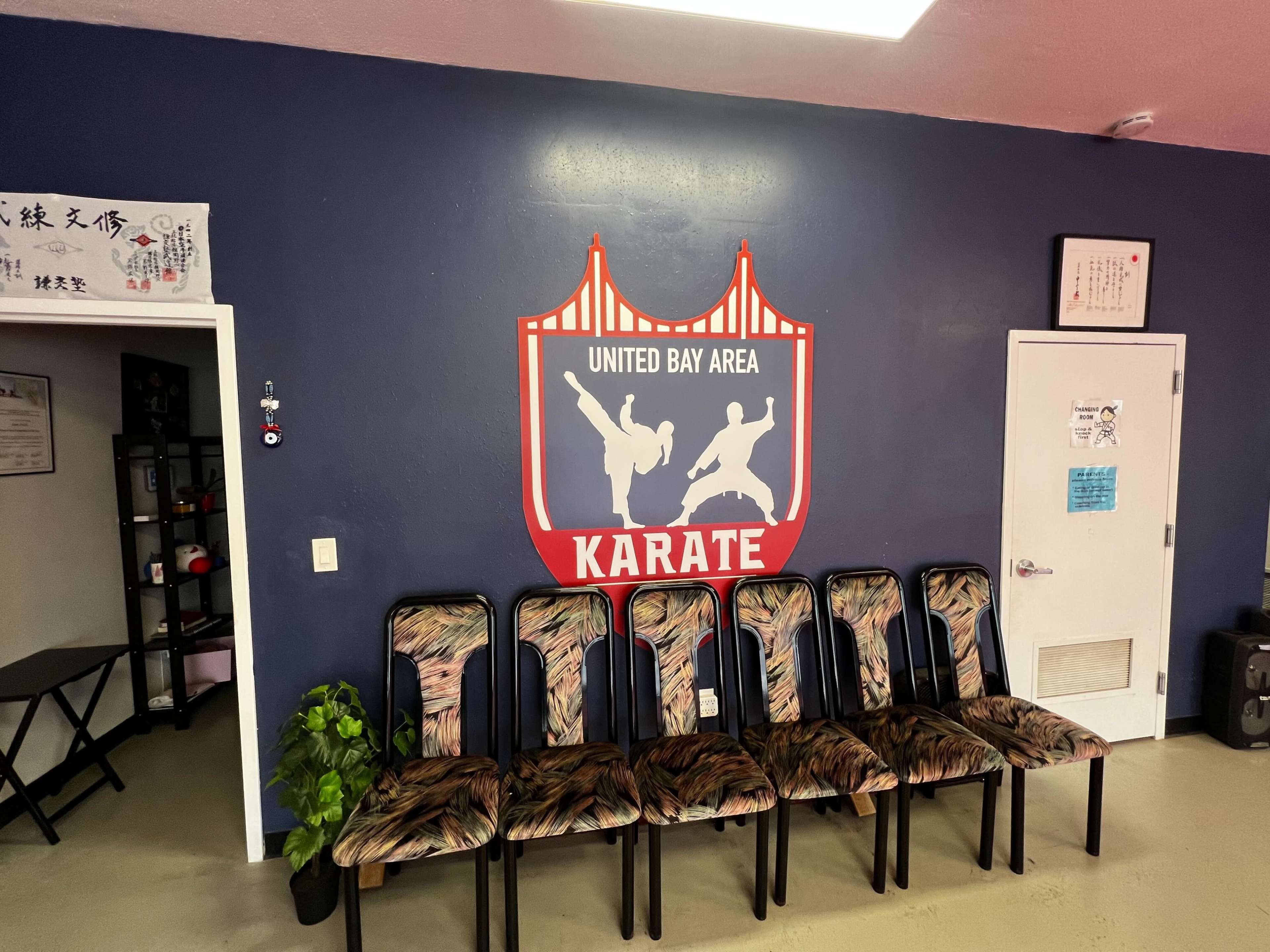 A karate studio with a graphic logo on the wall featuring two martial artists and a row of patterned chairs in front of it.