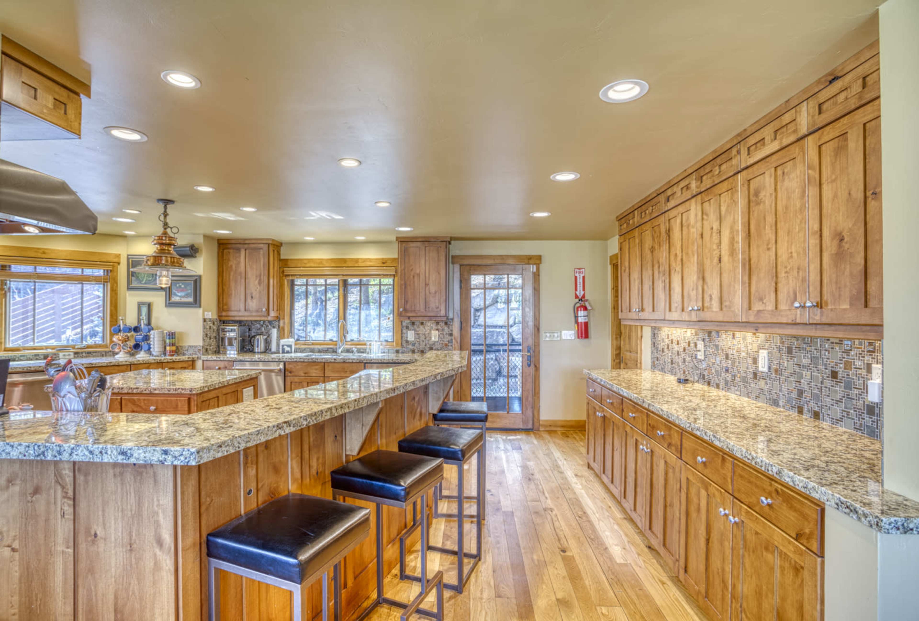 A spacious kitchen with wooden cabinets, granite countertops, and a central island with black bar stools.