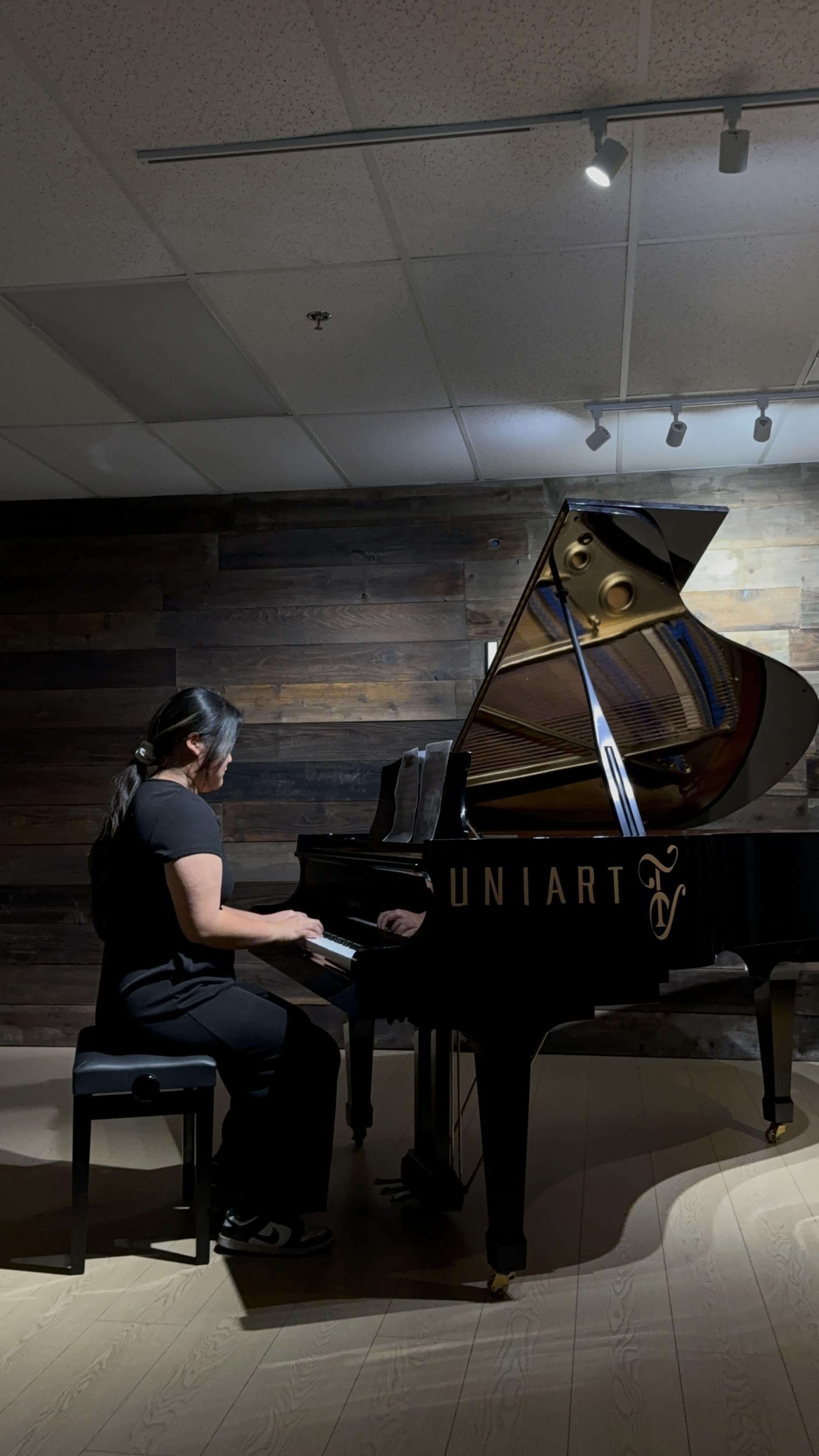 A person is playing a grand piano in a dimly lit room with wooden walls.