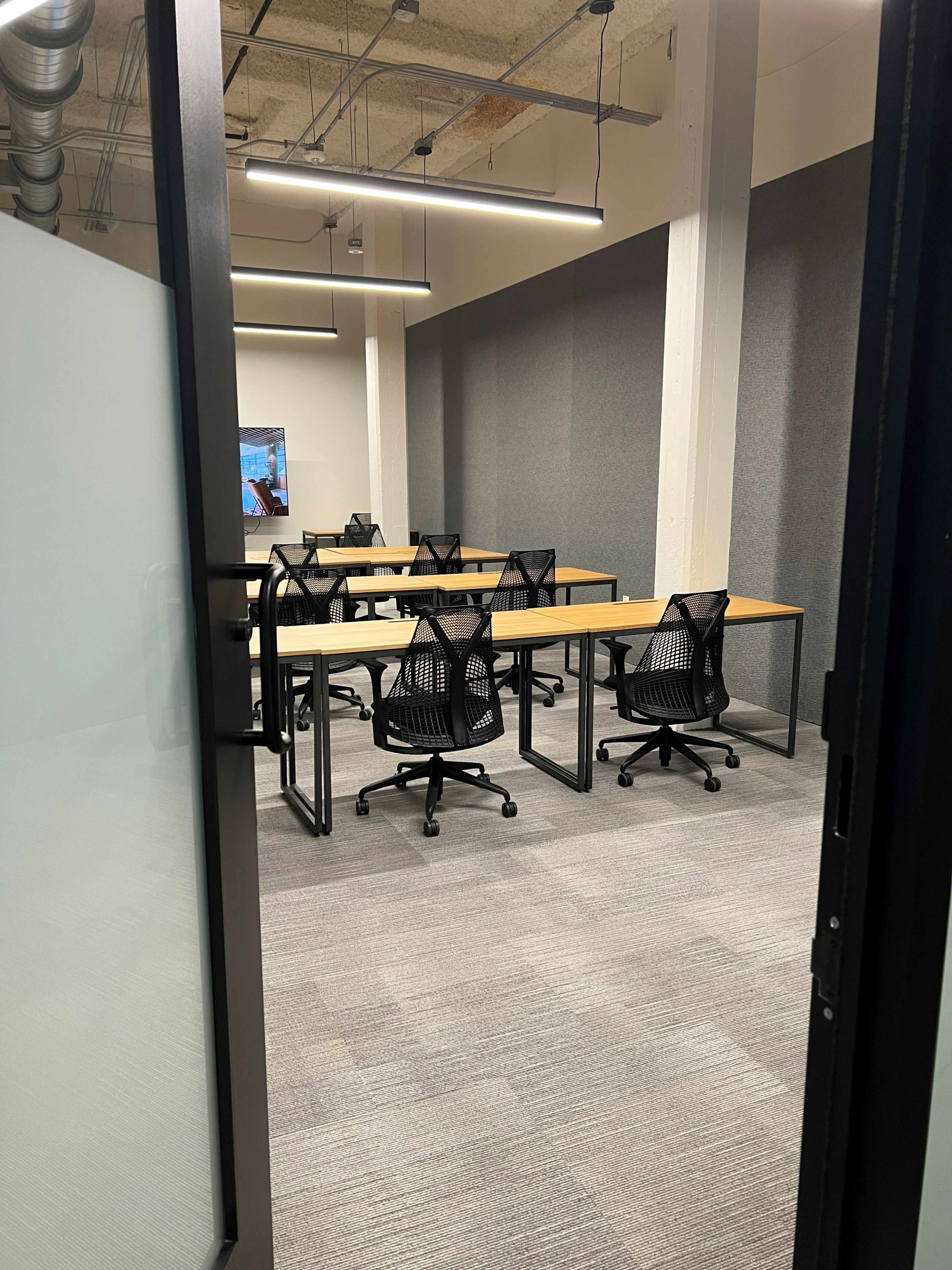 A modern conference room with several tables and black mesh chairs arranged neatly on a carpeted floor.