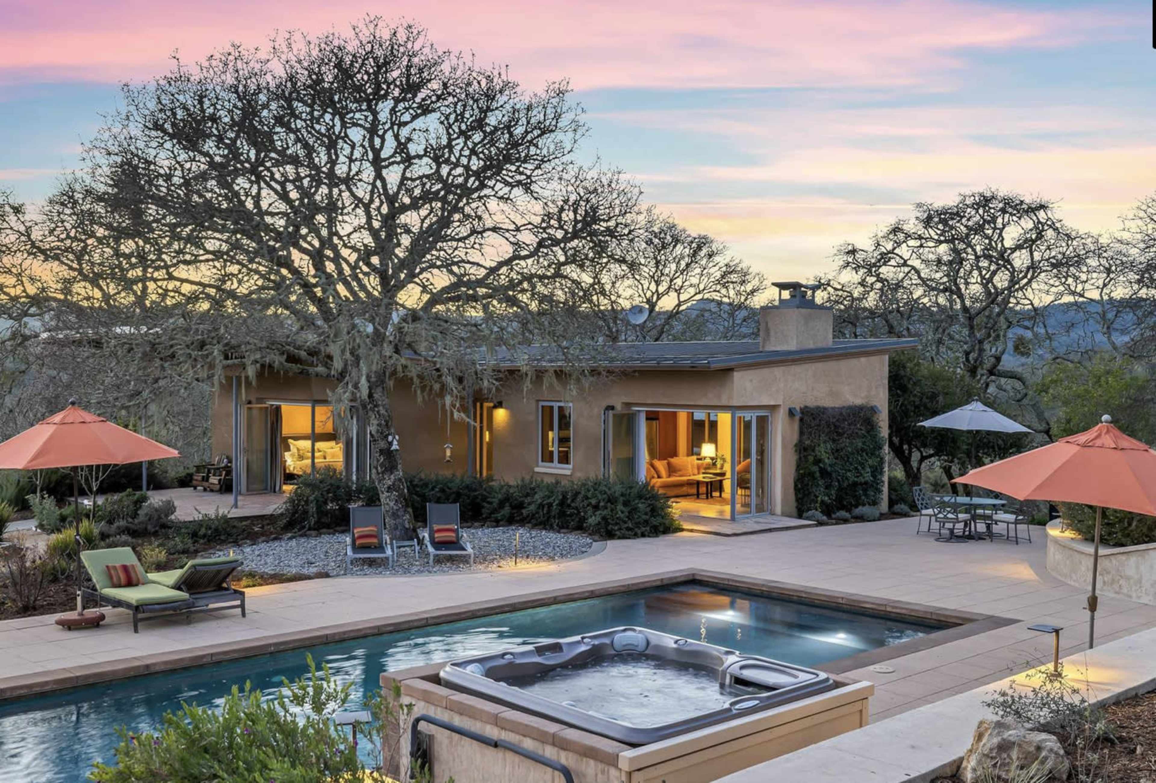 A modern house with a pool and hot tub, surrounded by landscaped gardens and patio furniture at sunset.