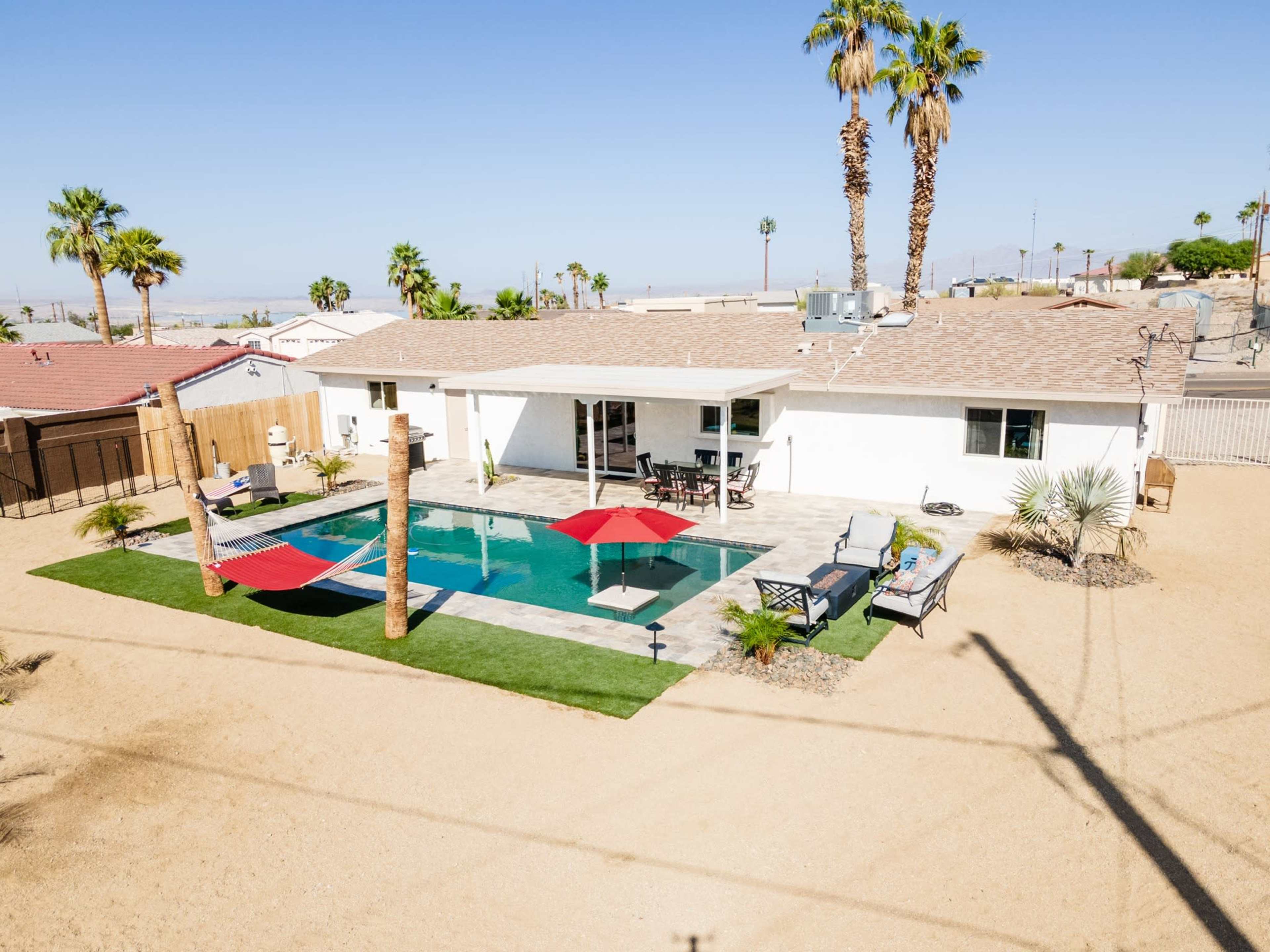 A modern home with a pool is surrounded by palm trees and a landscaped yard in a desert setting.