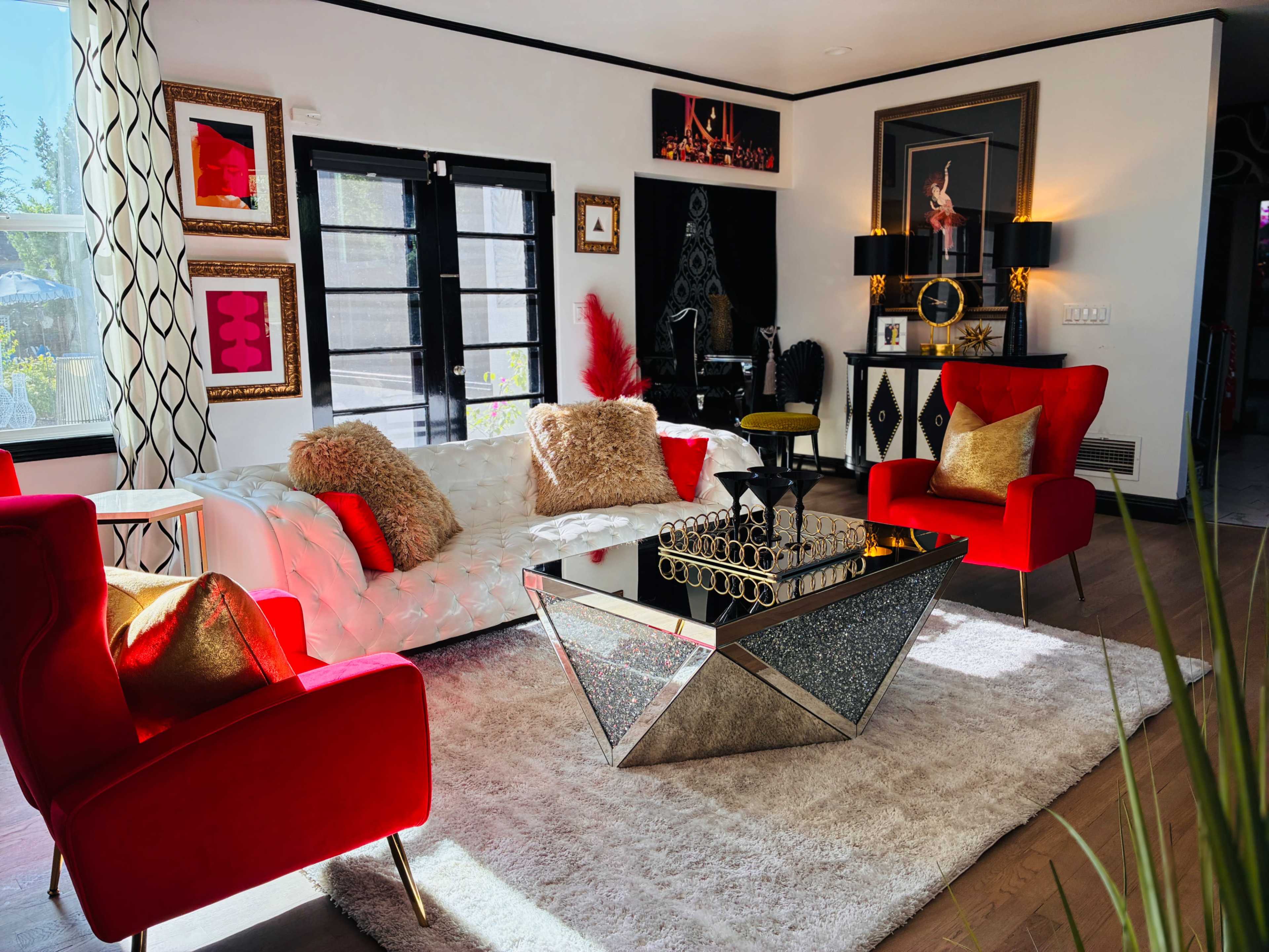 The image shows a stylish living room featuring a white sectional sofa and two red chairs, with a glass coffee table on a large area rug.