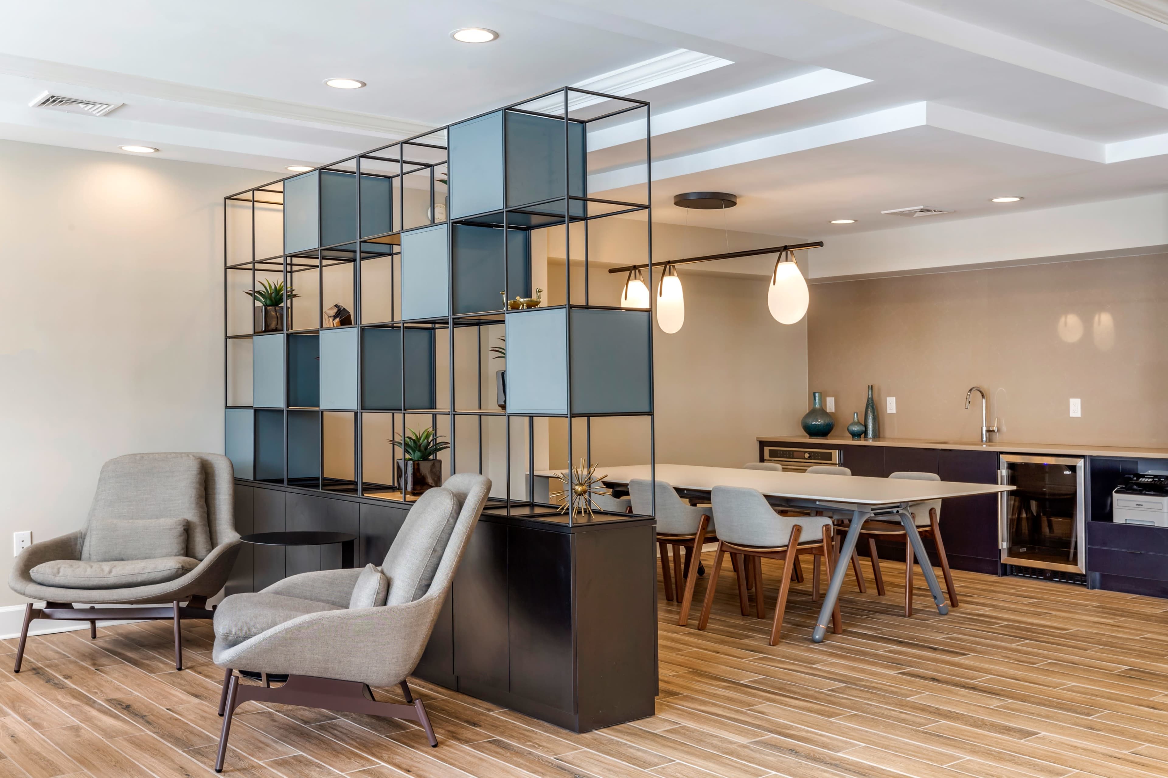 A modern interior space featuring a dining area with a table and chairs, a shelving unit, and two comfortable armchairs.