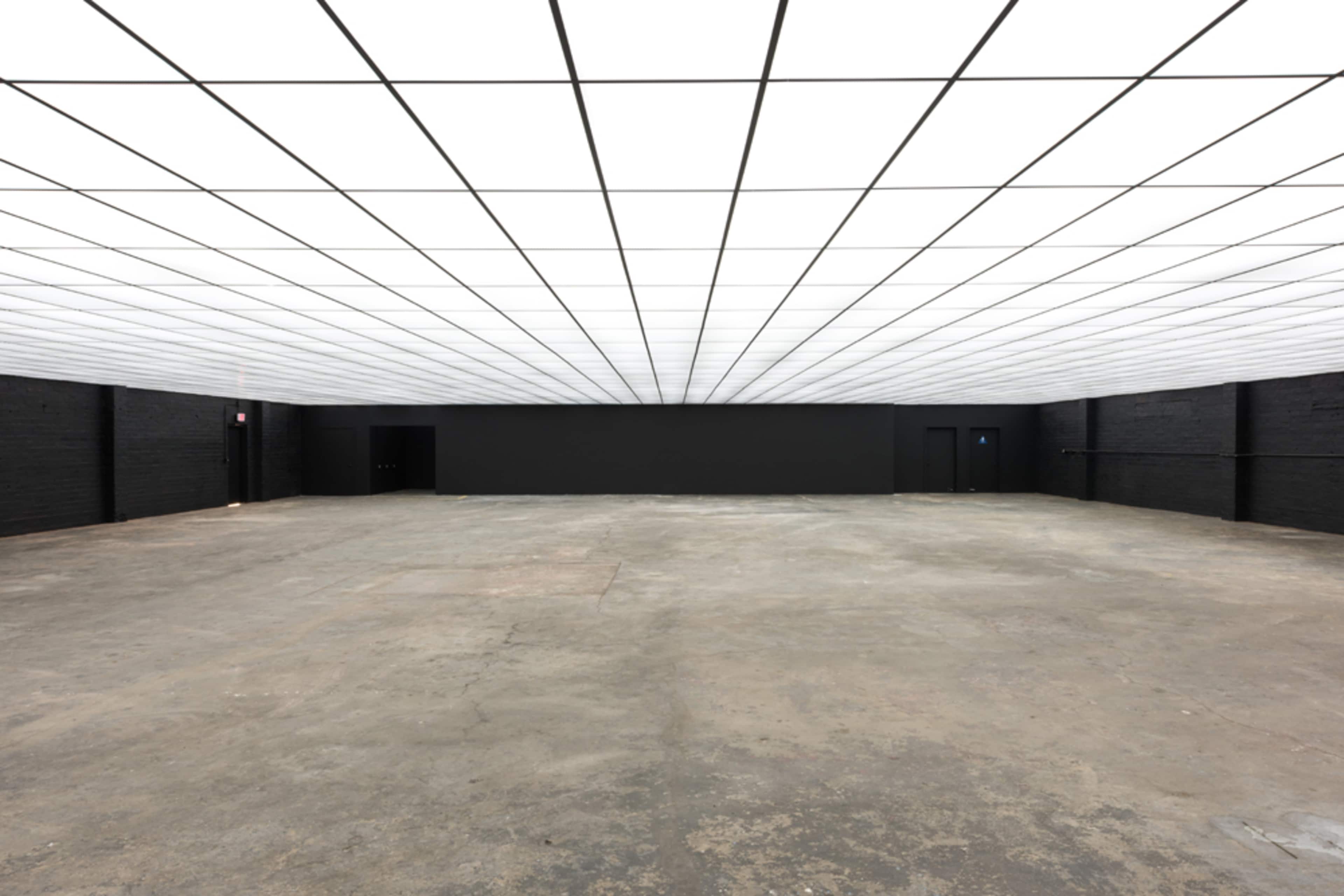 A spacious, empty room with a grid-patterned ceiling and dark walls.