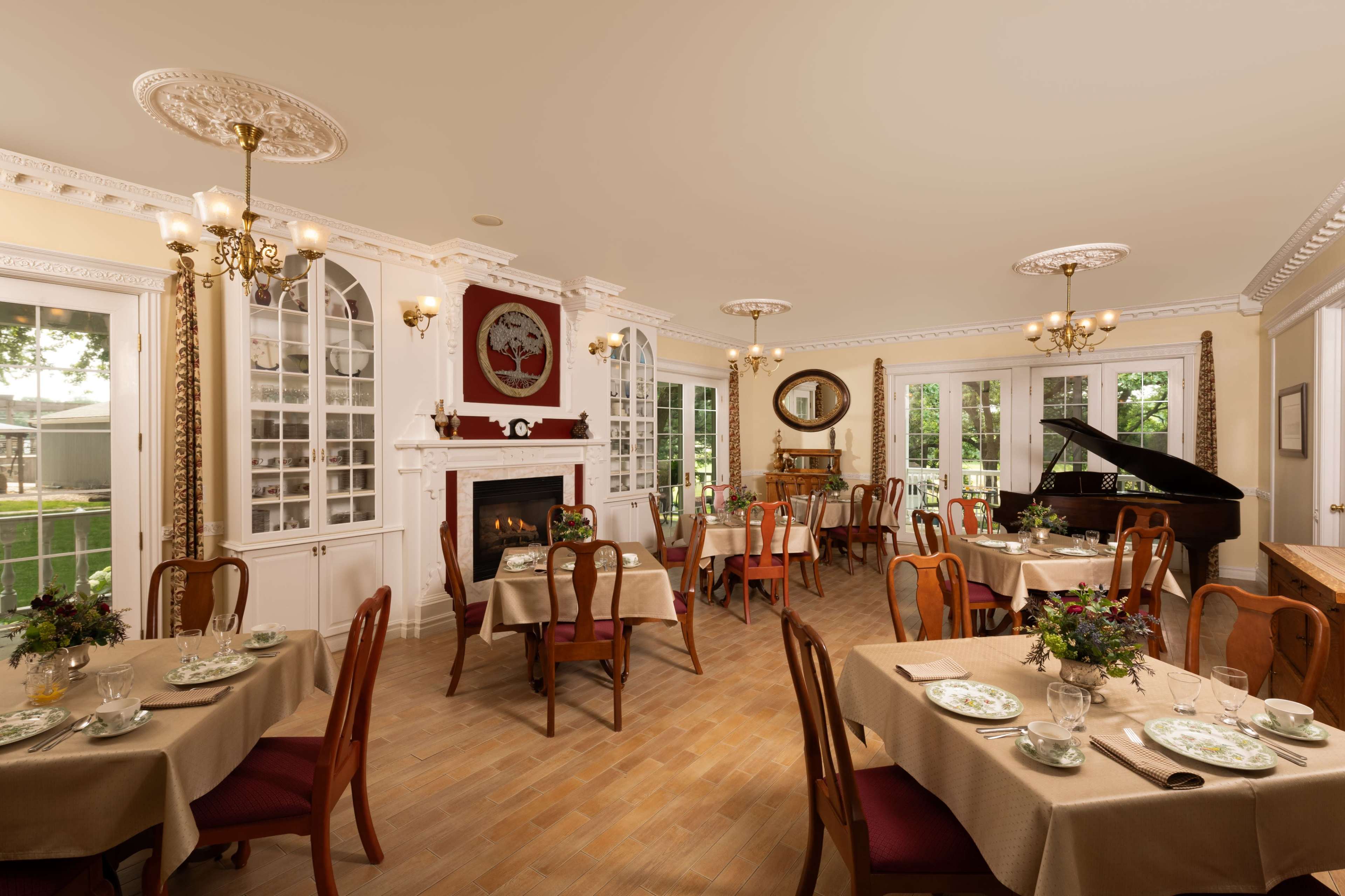 The image depicts a well-furnished dining room with elegantly set tables, a fireplace, and a grand piano.