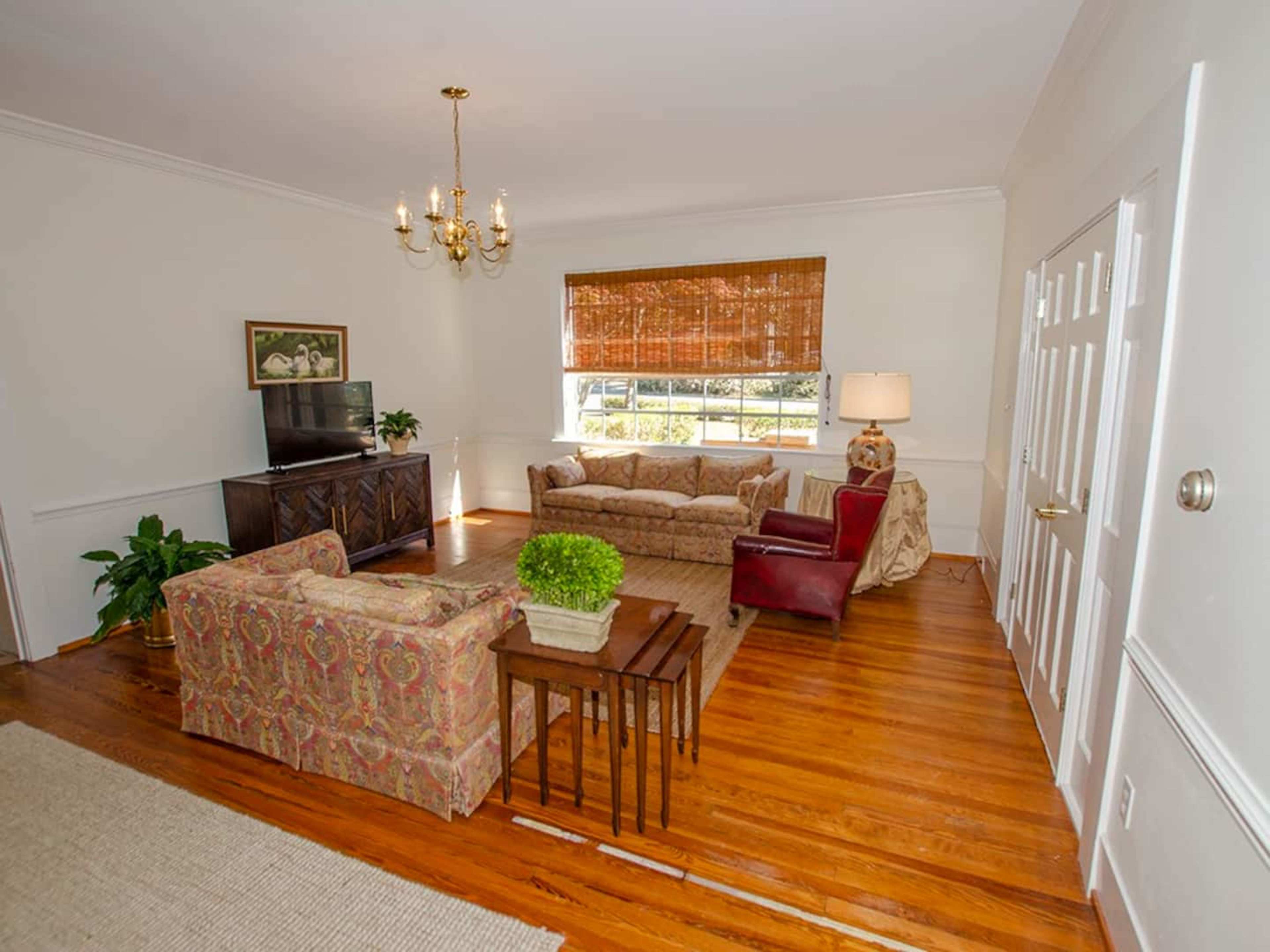 The living room features a television on a cabinet, a sofa set, a table, and a window with natural light.