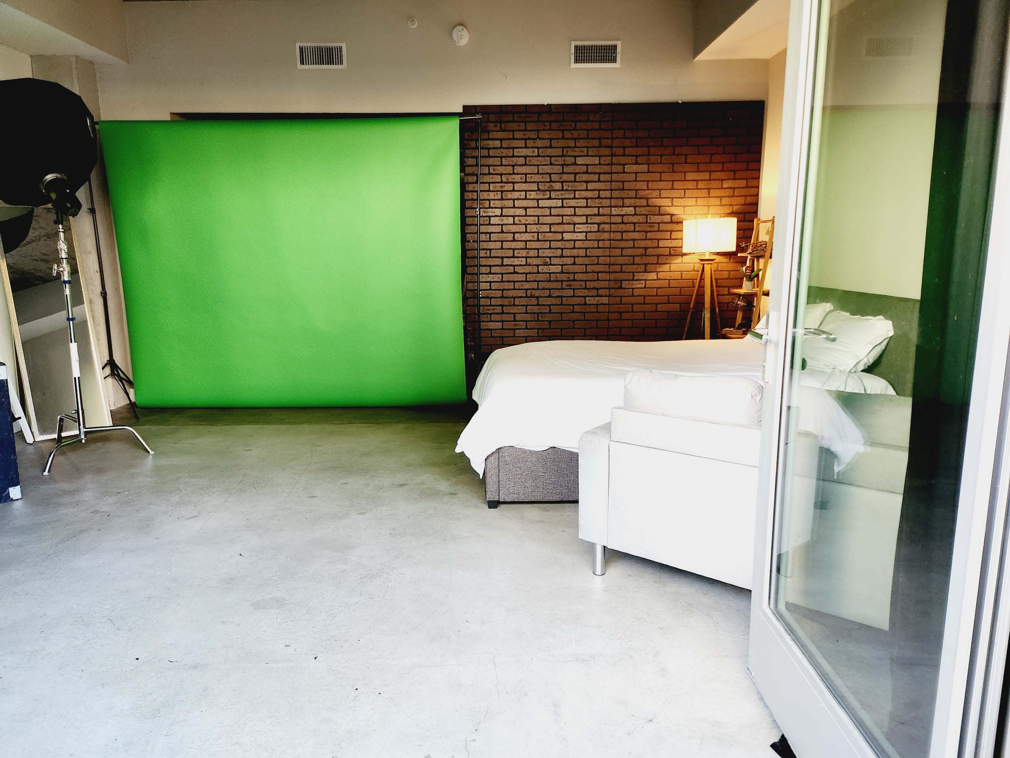 The image shows an indoor space with a green screen backdrop, a bed, a lamp, and a light-colored armchair.
