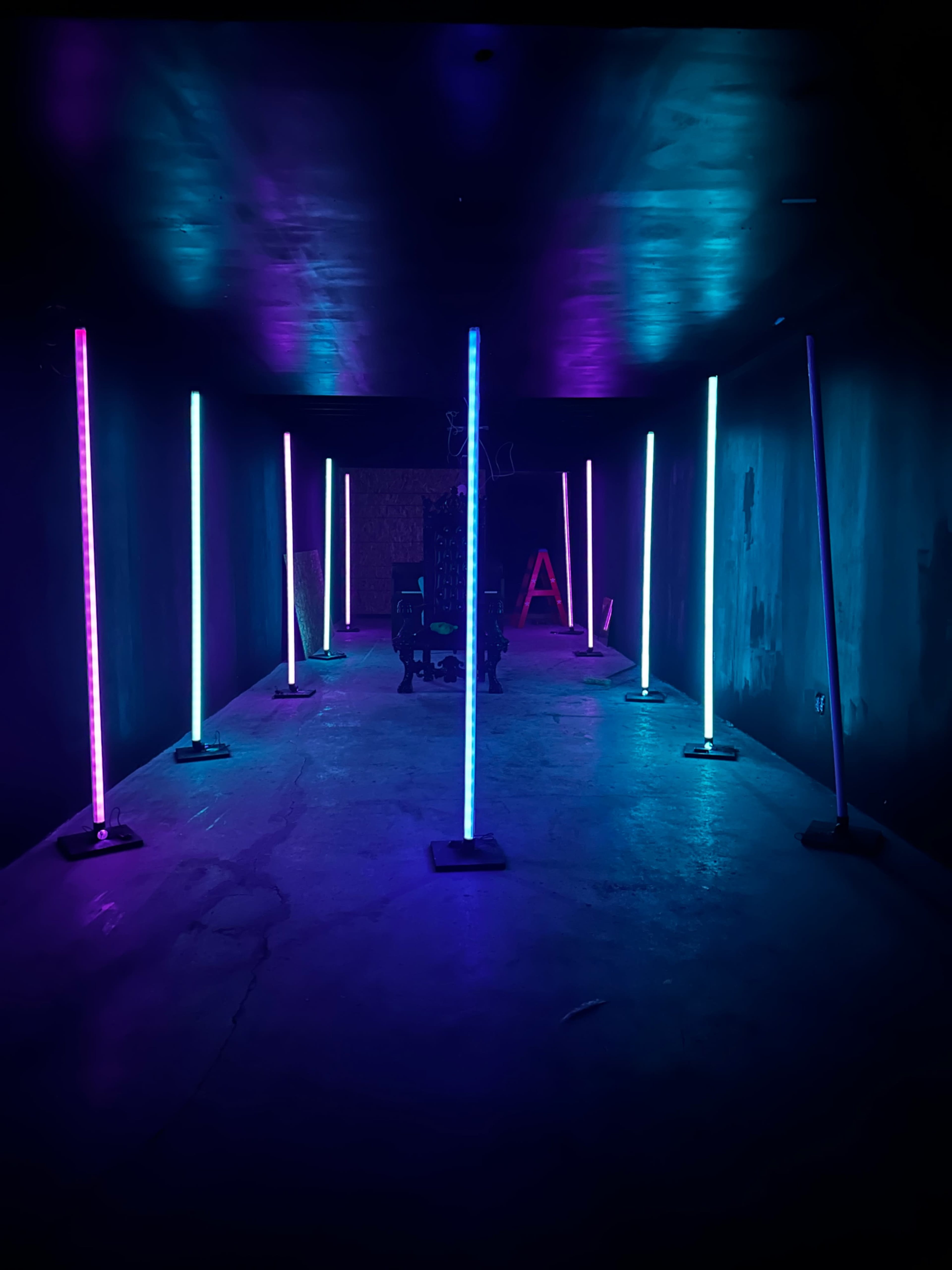 A dimly lit corridor lined with vertical light strips in shades of blue and purple.
