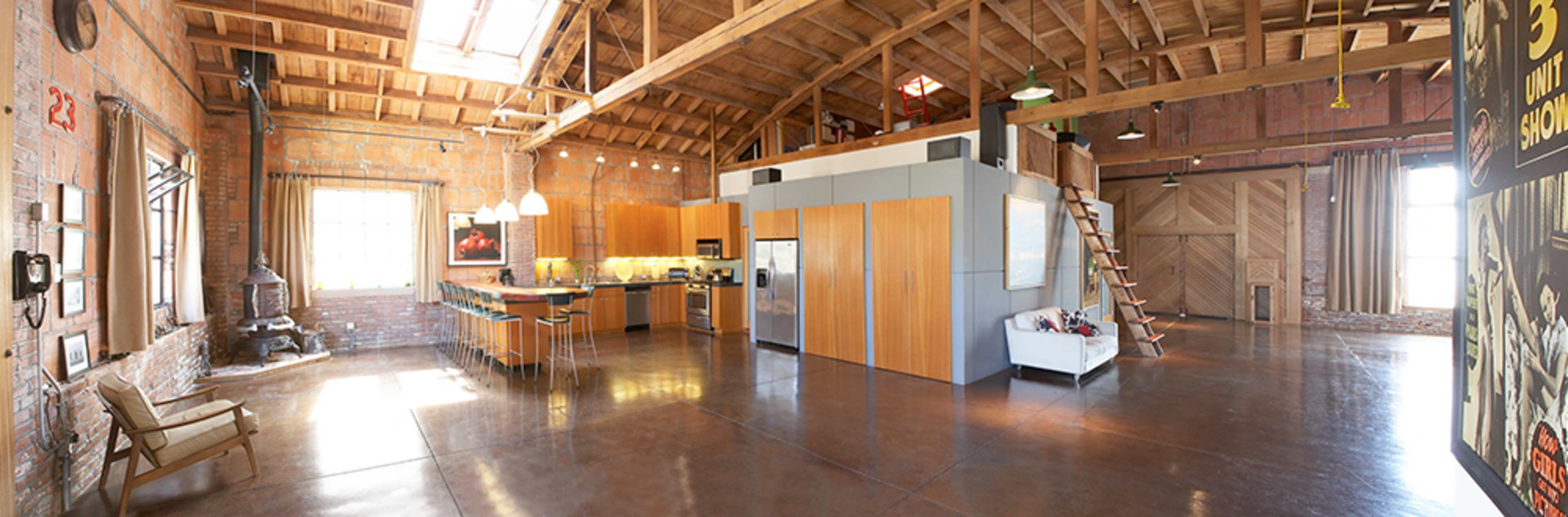 A spacious, open-concept loft with exposed brick walls, a modern kitchen, and a wooden staircase leading to a lofted area.