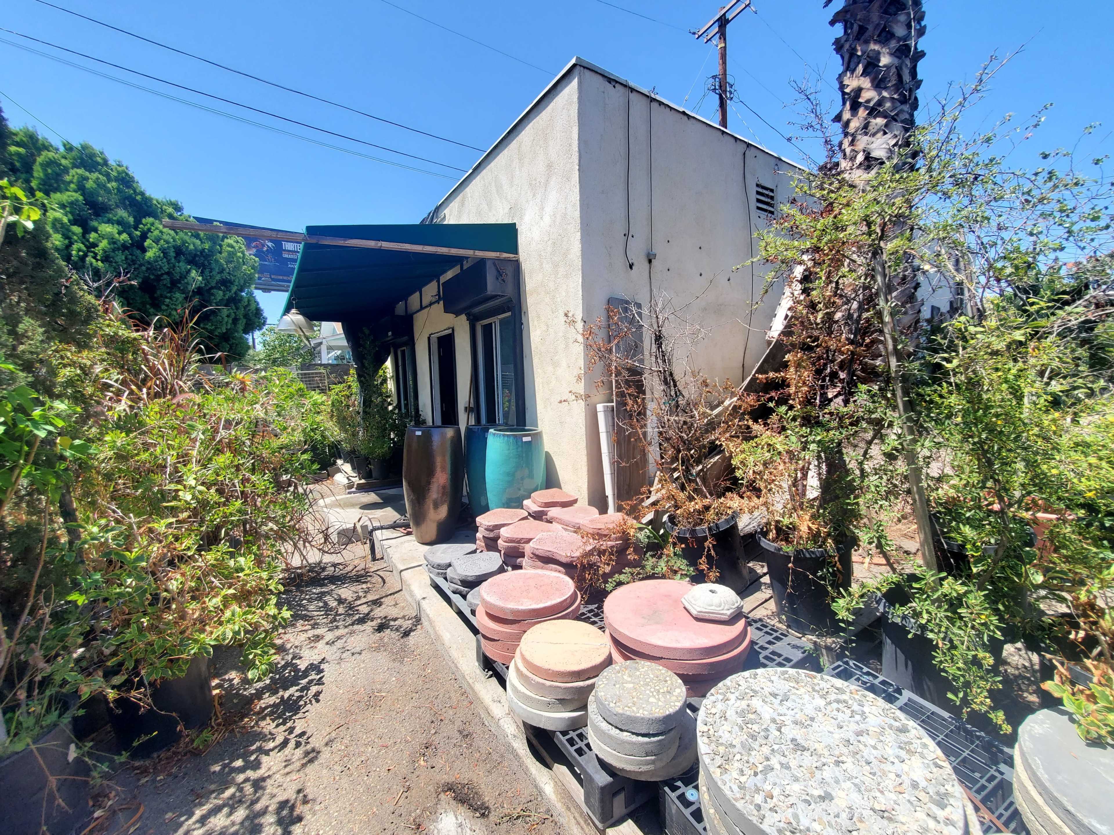 A narrow path leads to a building surrounded by various potted plants and garden stones.