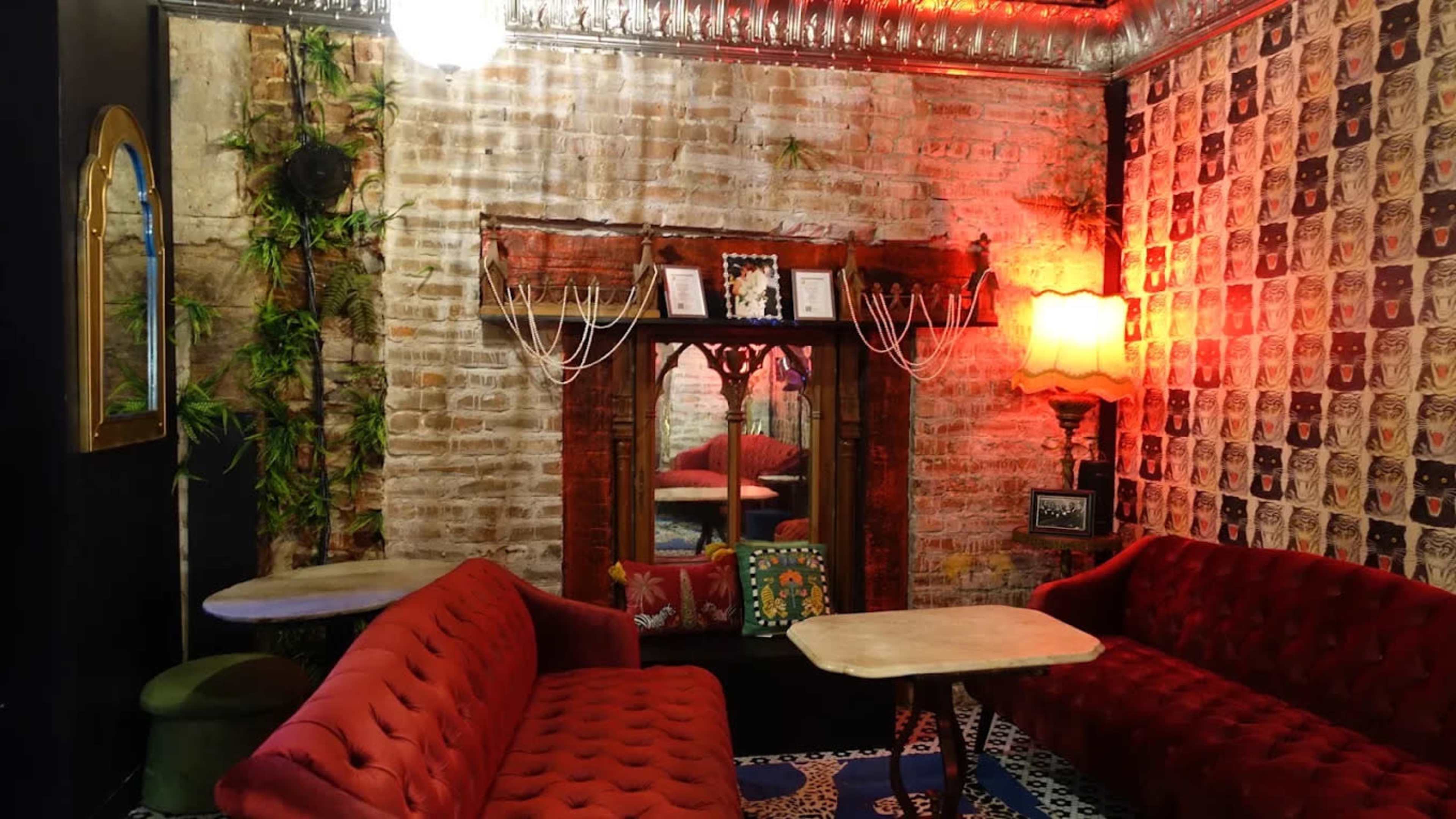 The image shows a cozy interior of a café or lounge with exposed brick walls, vintage furniture, and warm lighting.