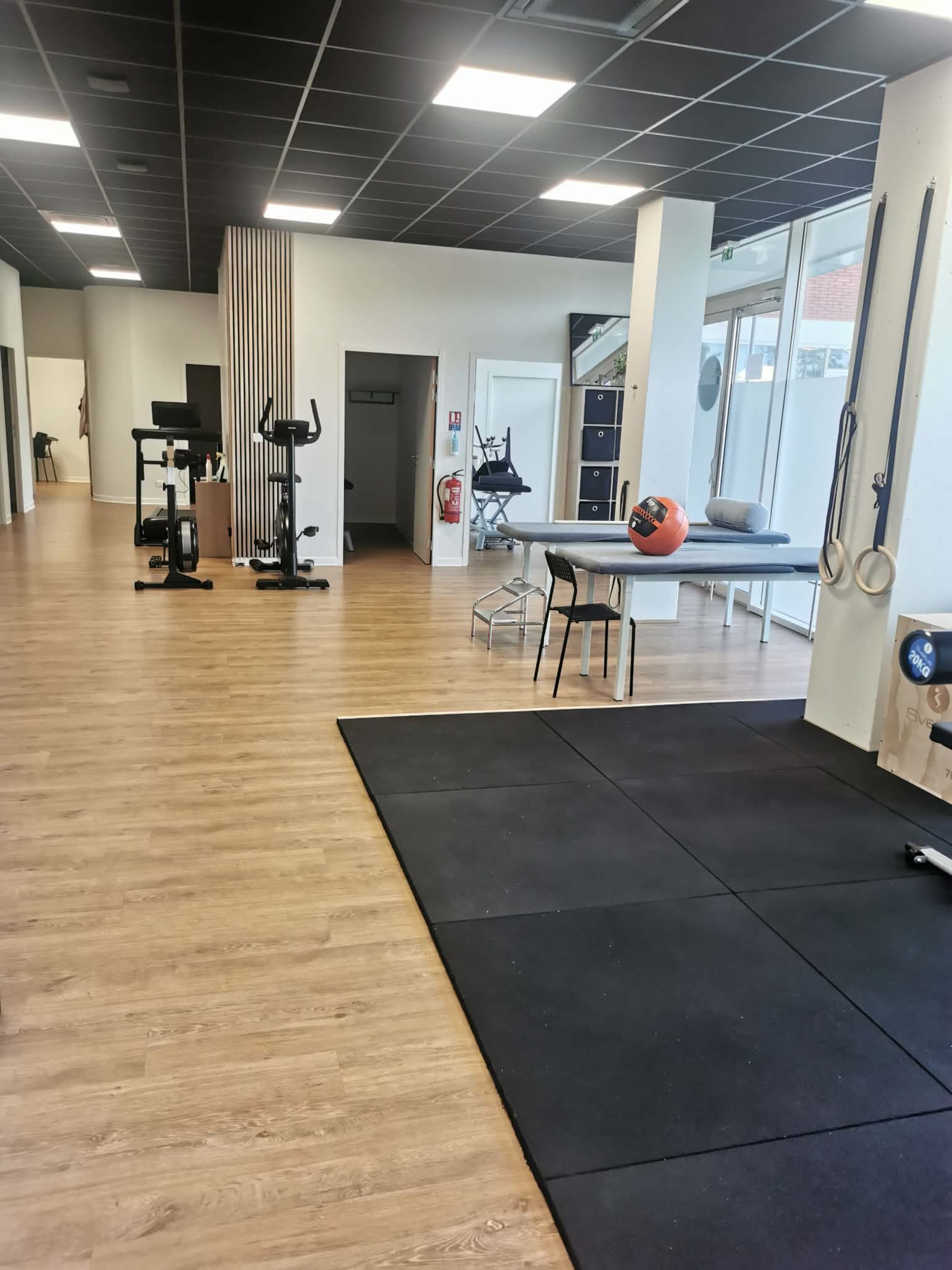 The image shows a modern fitness center with exercise equipment, wooden flooring, and well-lit spaces.