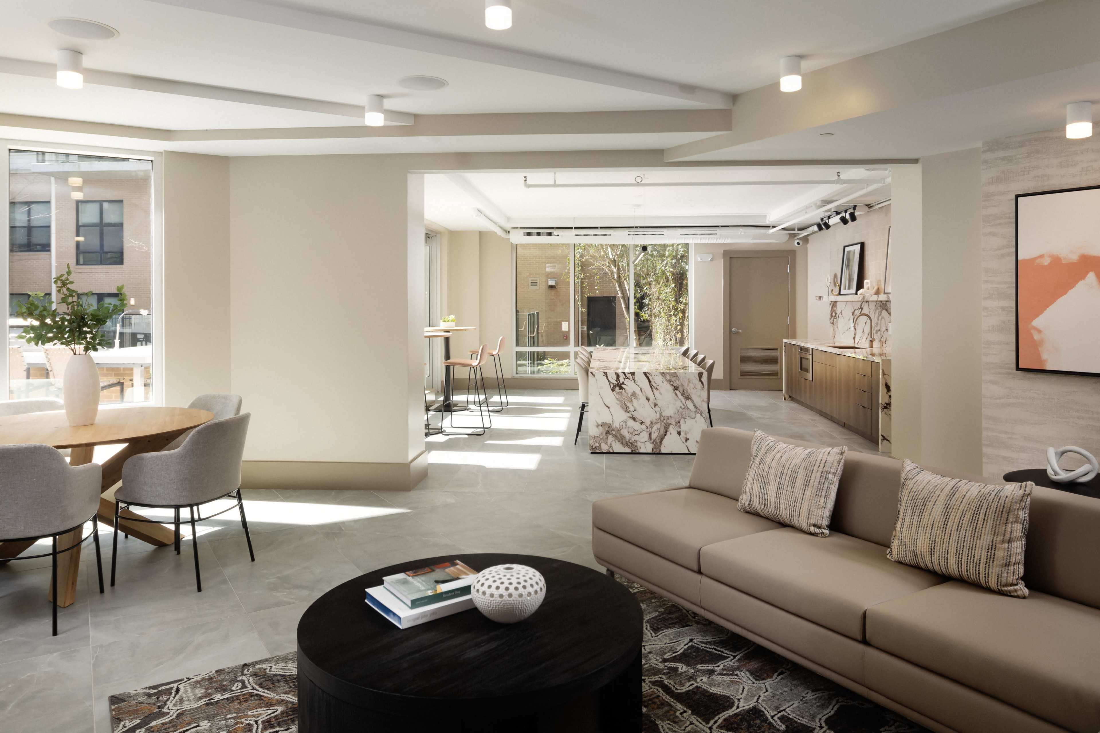 A modern, open-concept lounge area with a sectional sofa, a round coffee table, a dining space with chairs, and a kitchen in the background.