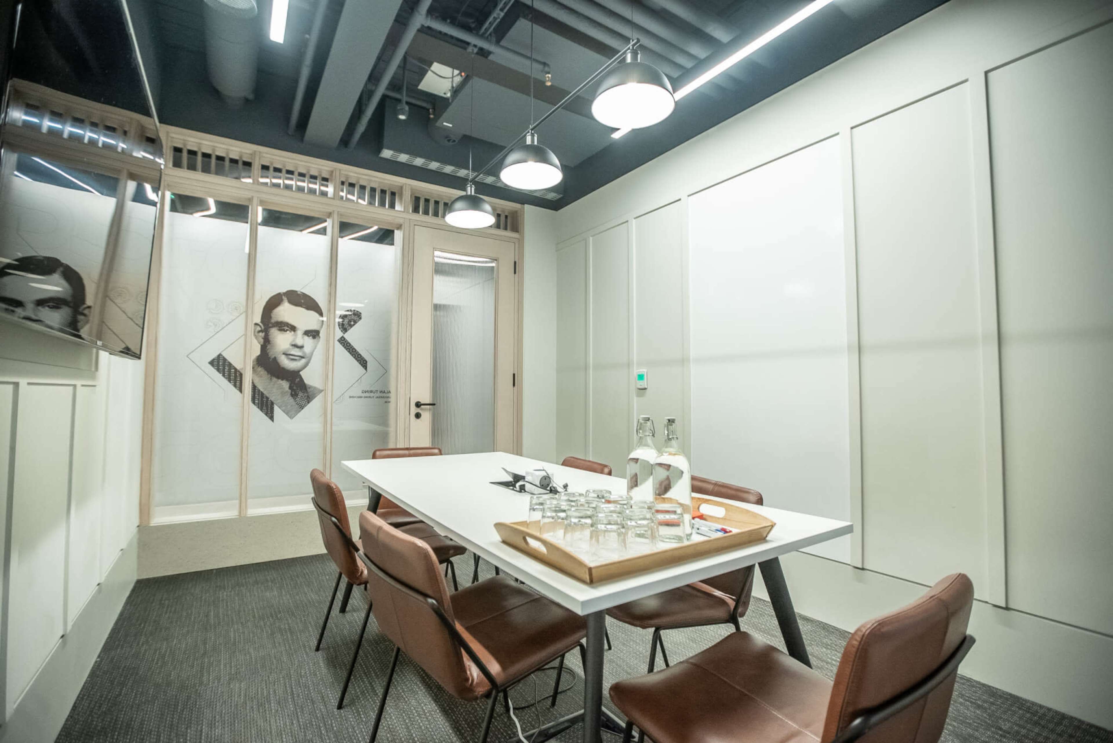 A modern meeting room features a white table surrounded by brown chairs and a glass wall with a portrait.