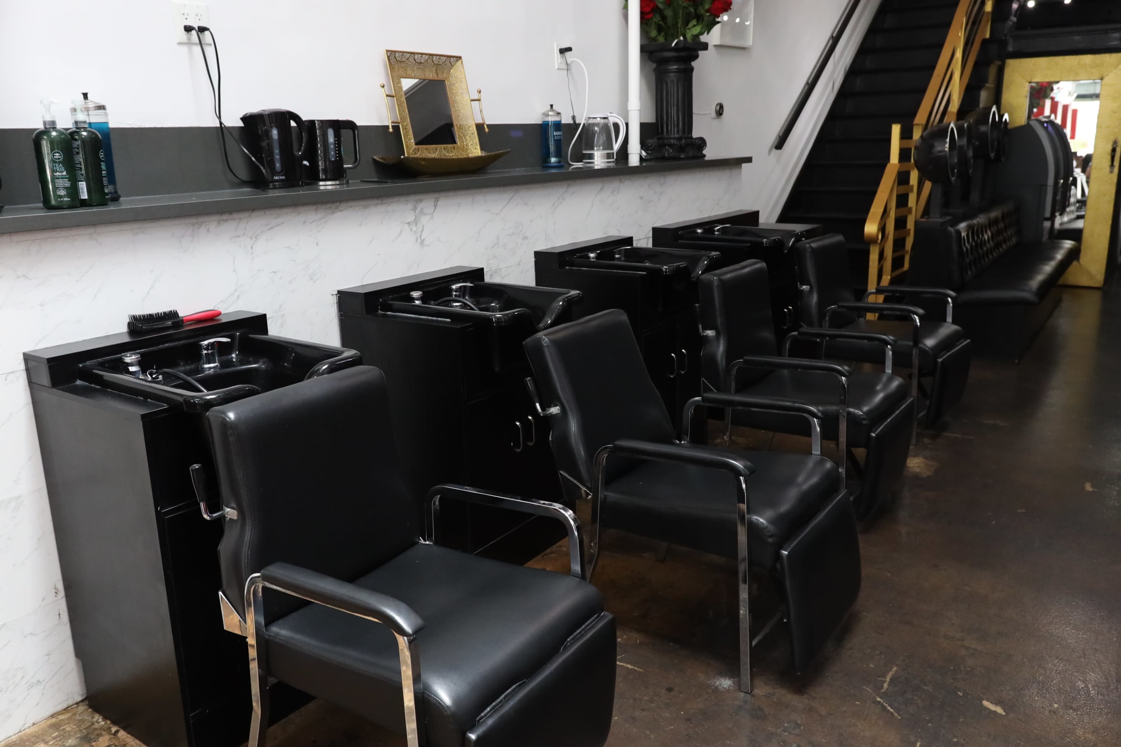A row of black salon chairs with attached wash basins in a hair salon.