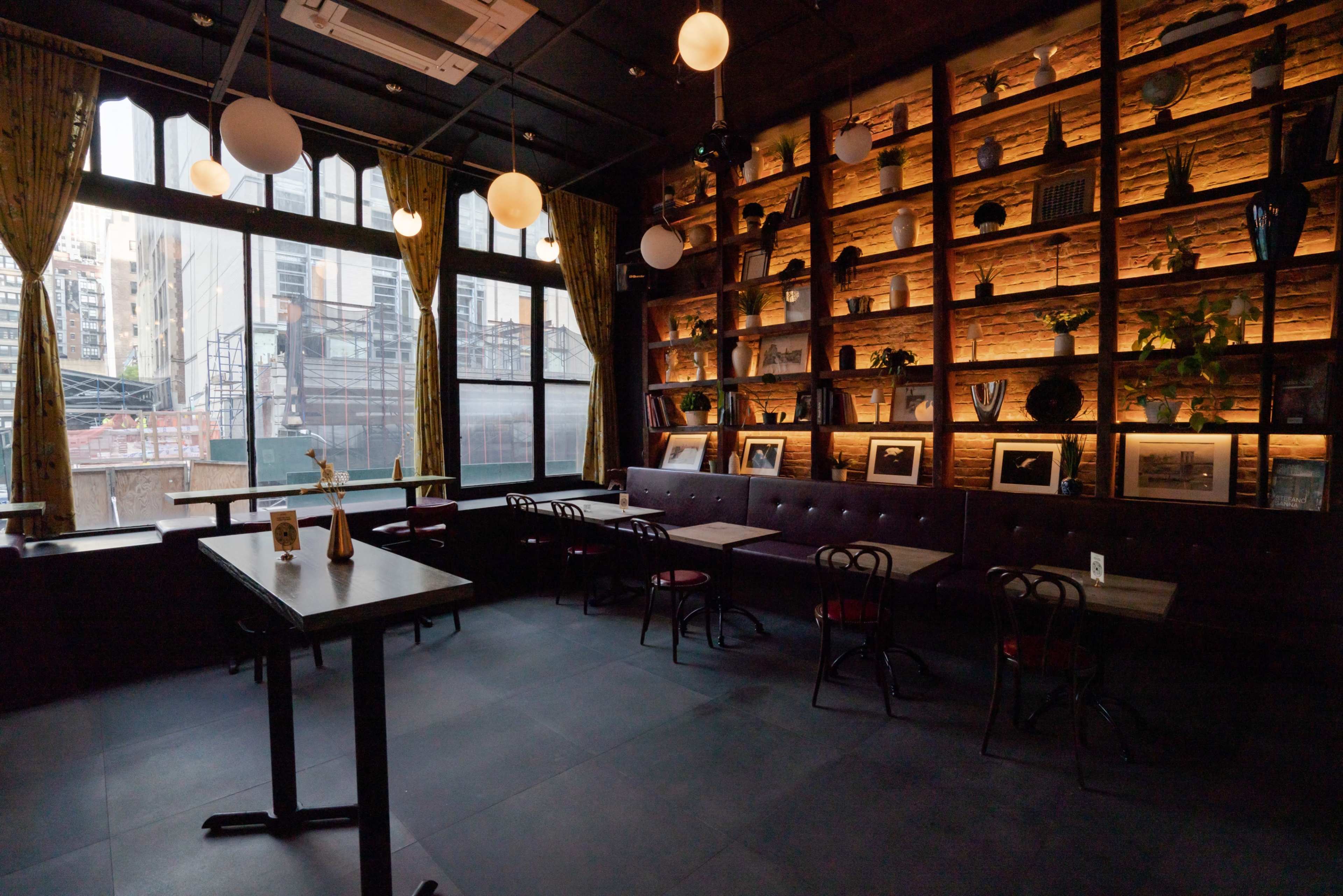 A dimly lit interior of a restaurant featuring wooden shelves filled with decorative items and framed pictures, with tables and chairs arranged for dining.