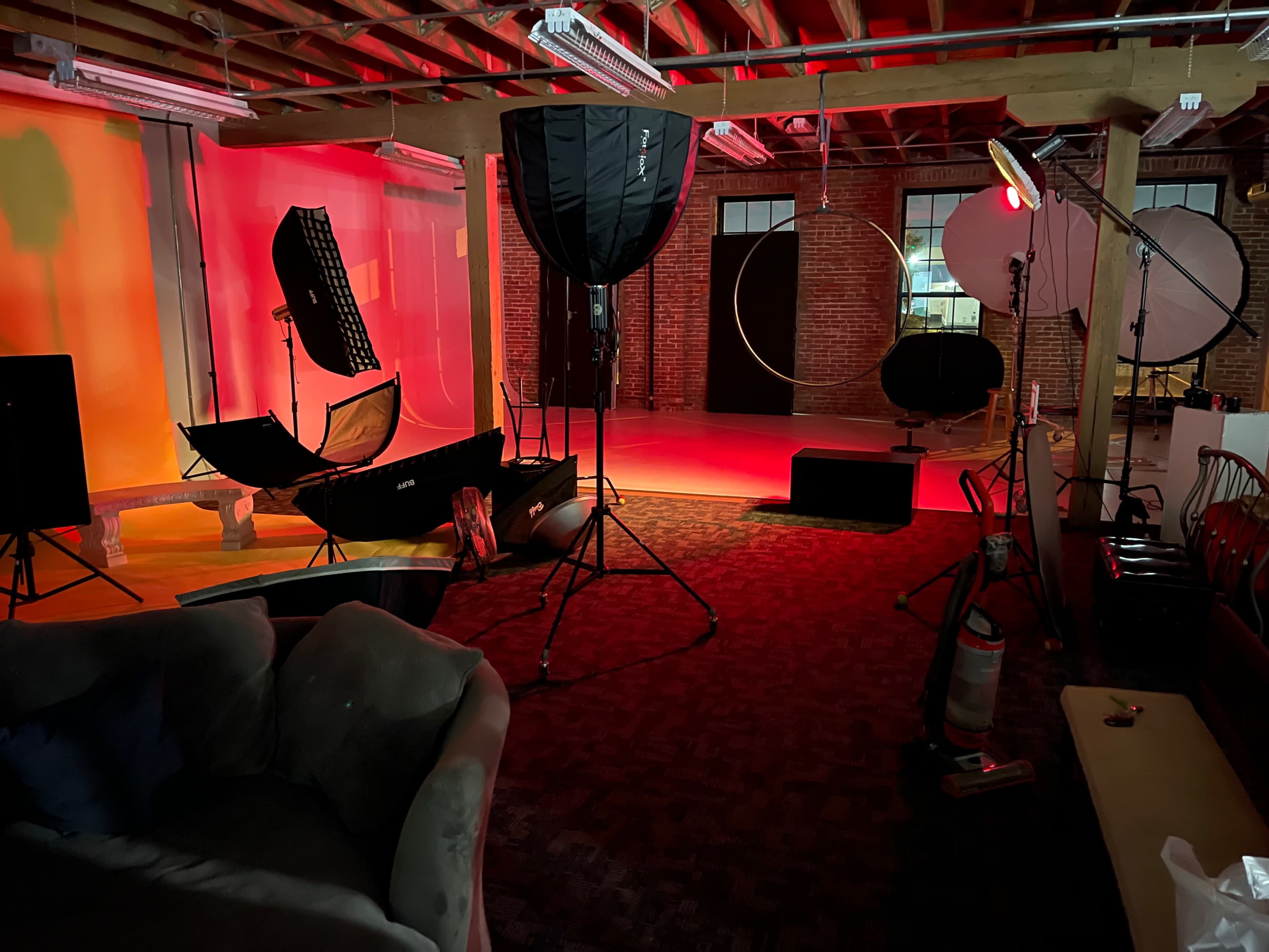 A photography studio setup with various lighting equipment and backdrops arranged in a spacious, industrial-style environment.