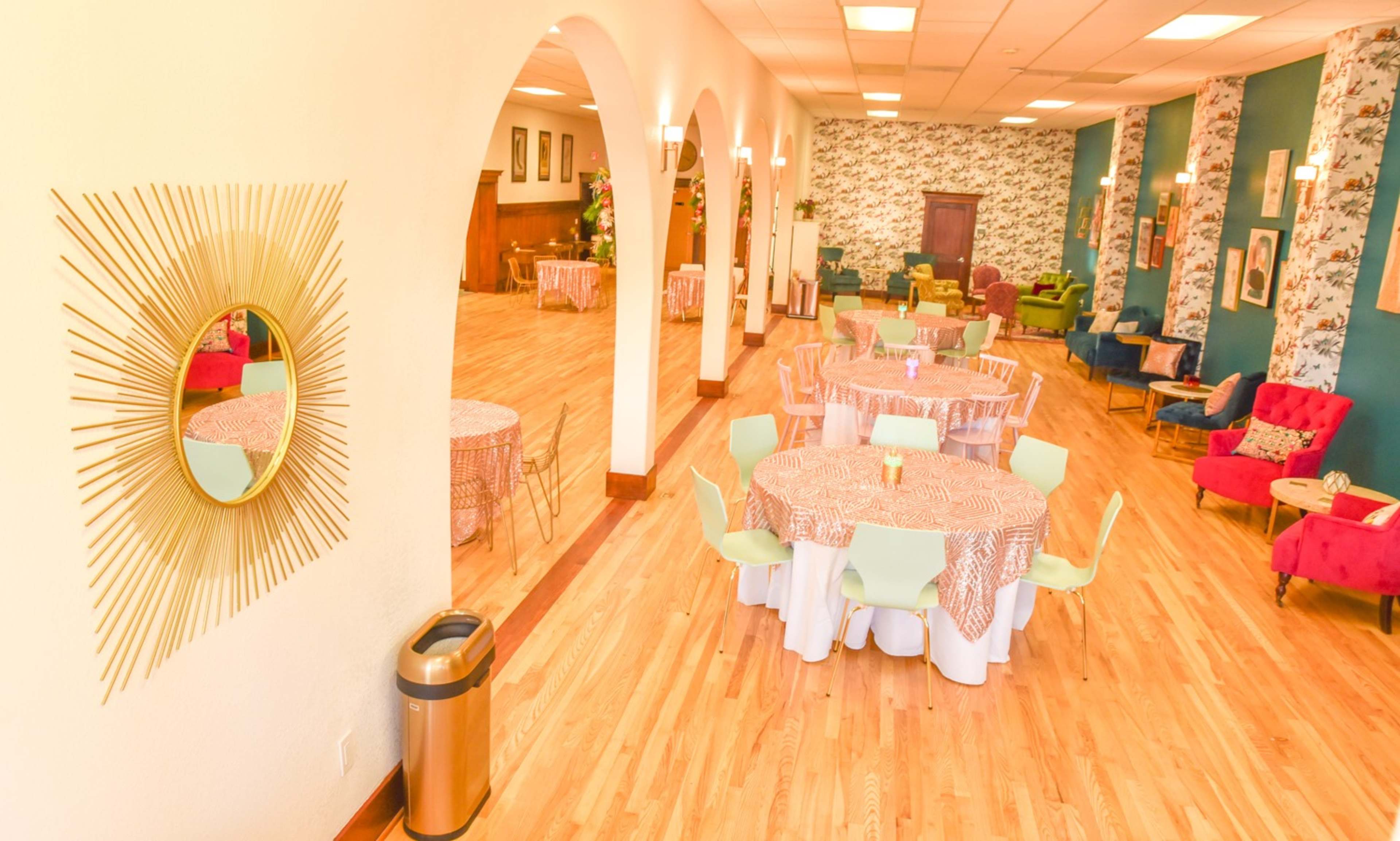 A spacious restaurant interior featuring several round tables with floral tablecloths and a variety of colorful seating arrangements.
