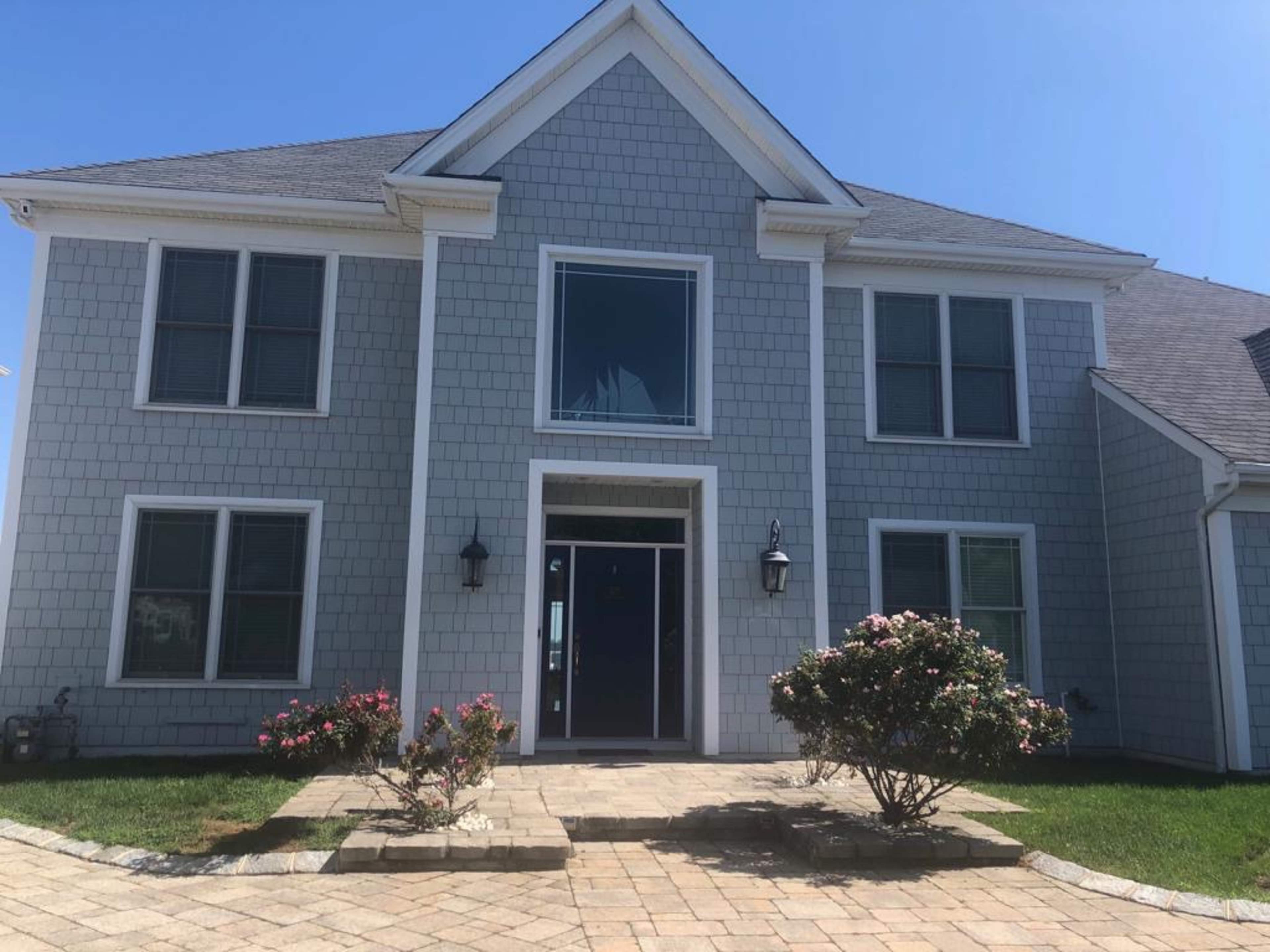 A two-story gray home with a shingle exterior, a central glass door, and a flower garden in front.