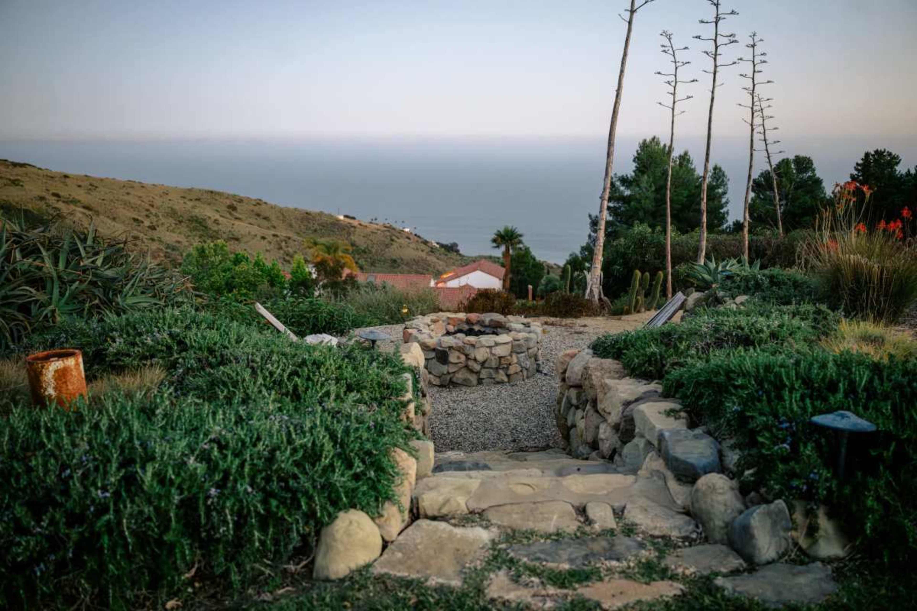 A stone pathway descends through landscaped greenery toward a view of the ocean in the distance.