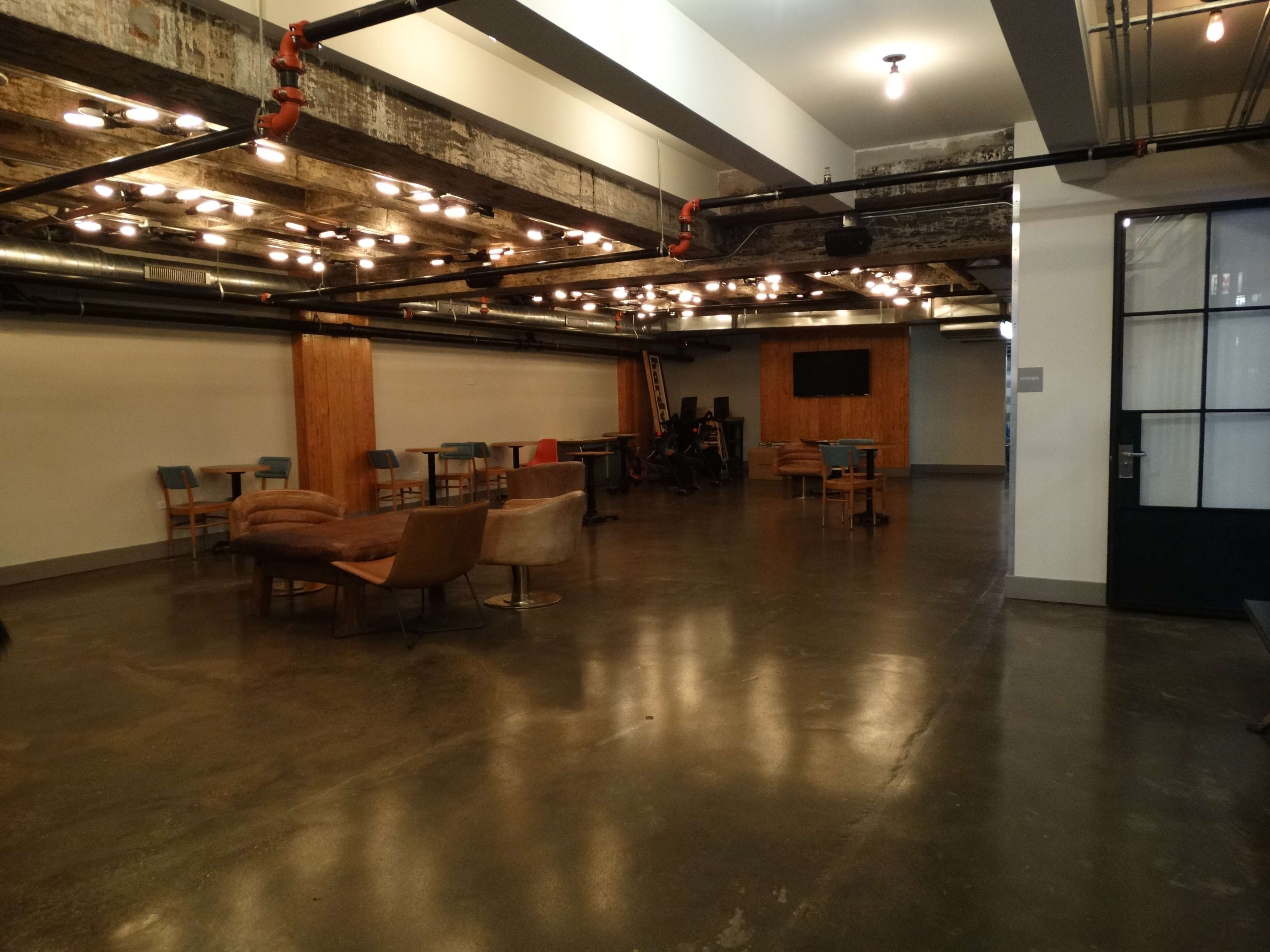 An industrial-style interior space with concrete floors, exposed beams, and various seating arrangements, including tables and chairs.