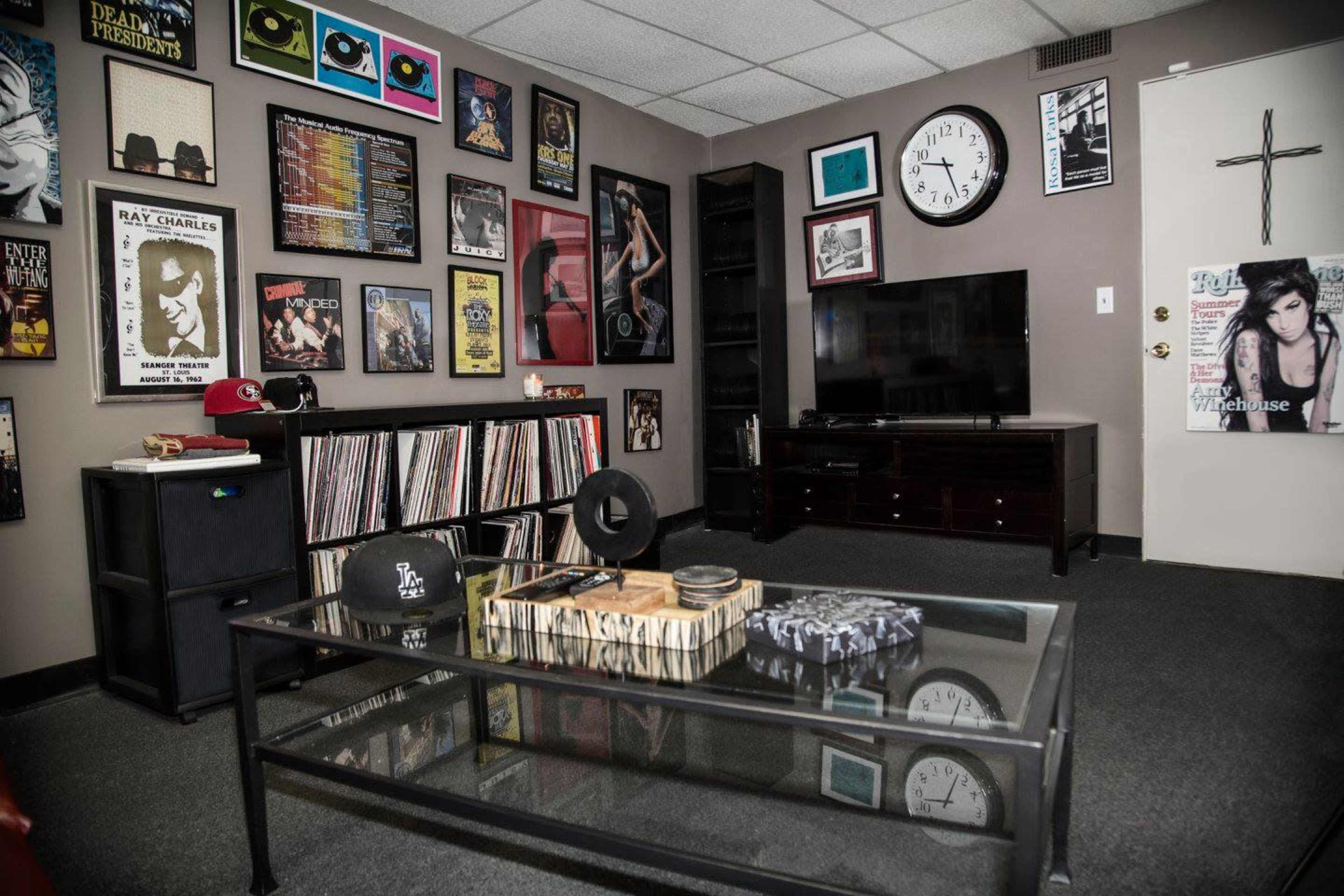 A room decorated with framed music posters and records, containing a television, a glass coffee table, and a black bookshelf.