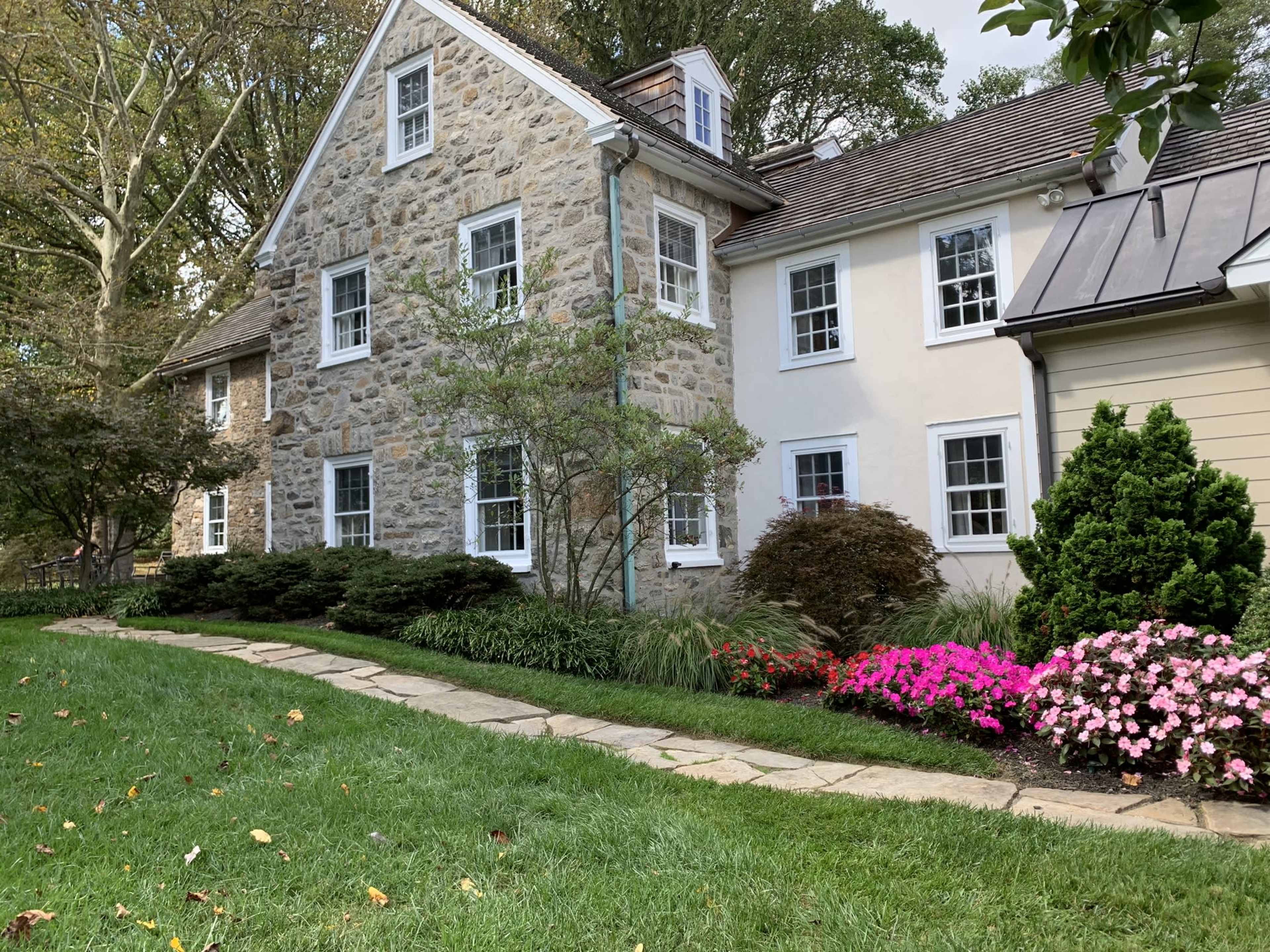 A two-story house with a stone exterior and a landscaped garden featuring a stone pathway and flowering plants.