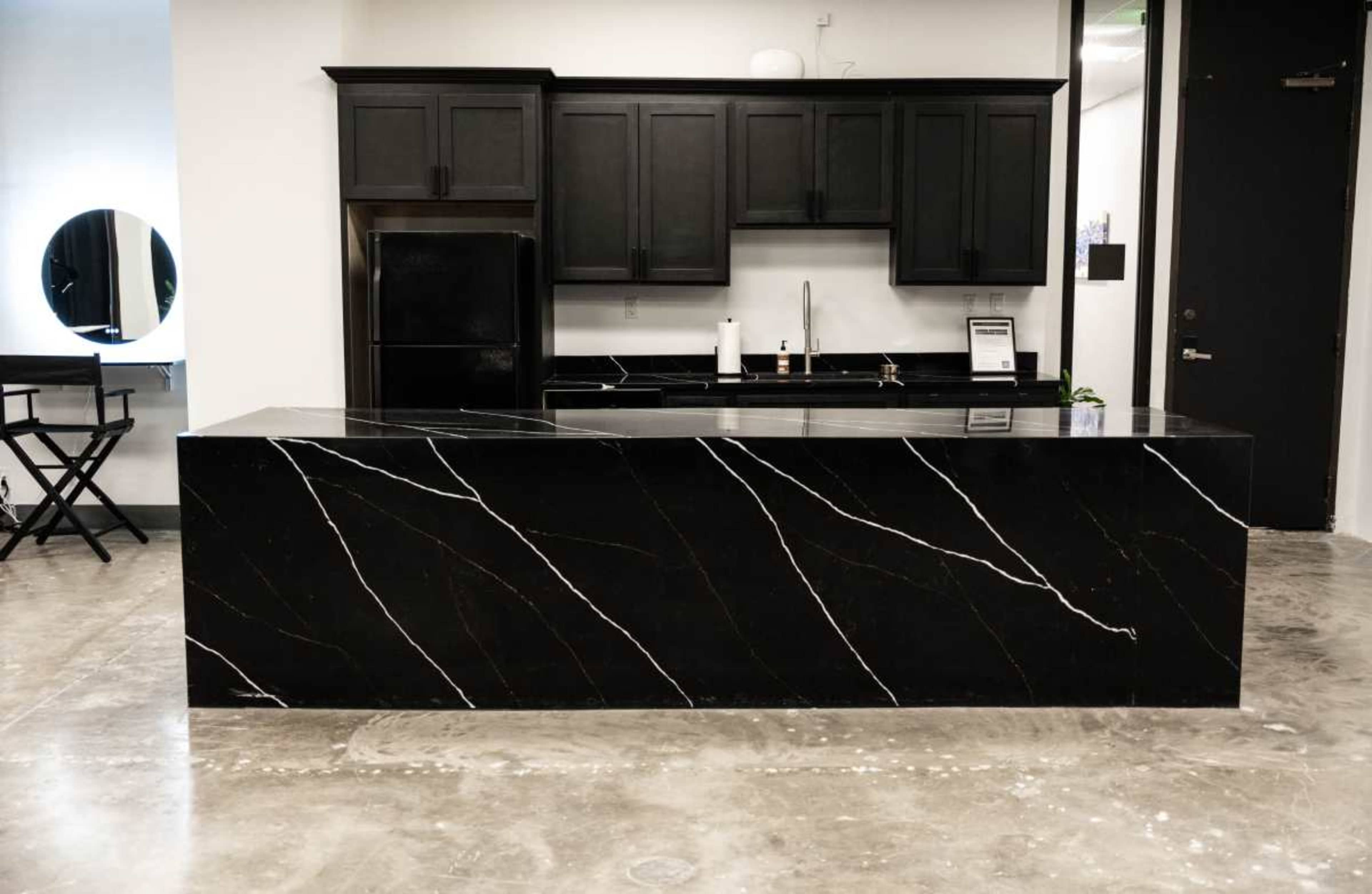 The image shows a modern kitchen featuring black cabinets and a large black stone countertop with white veins.