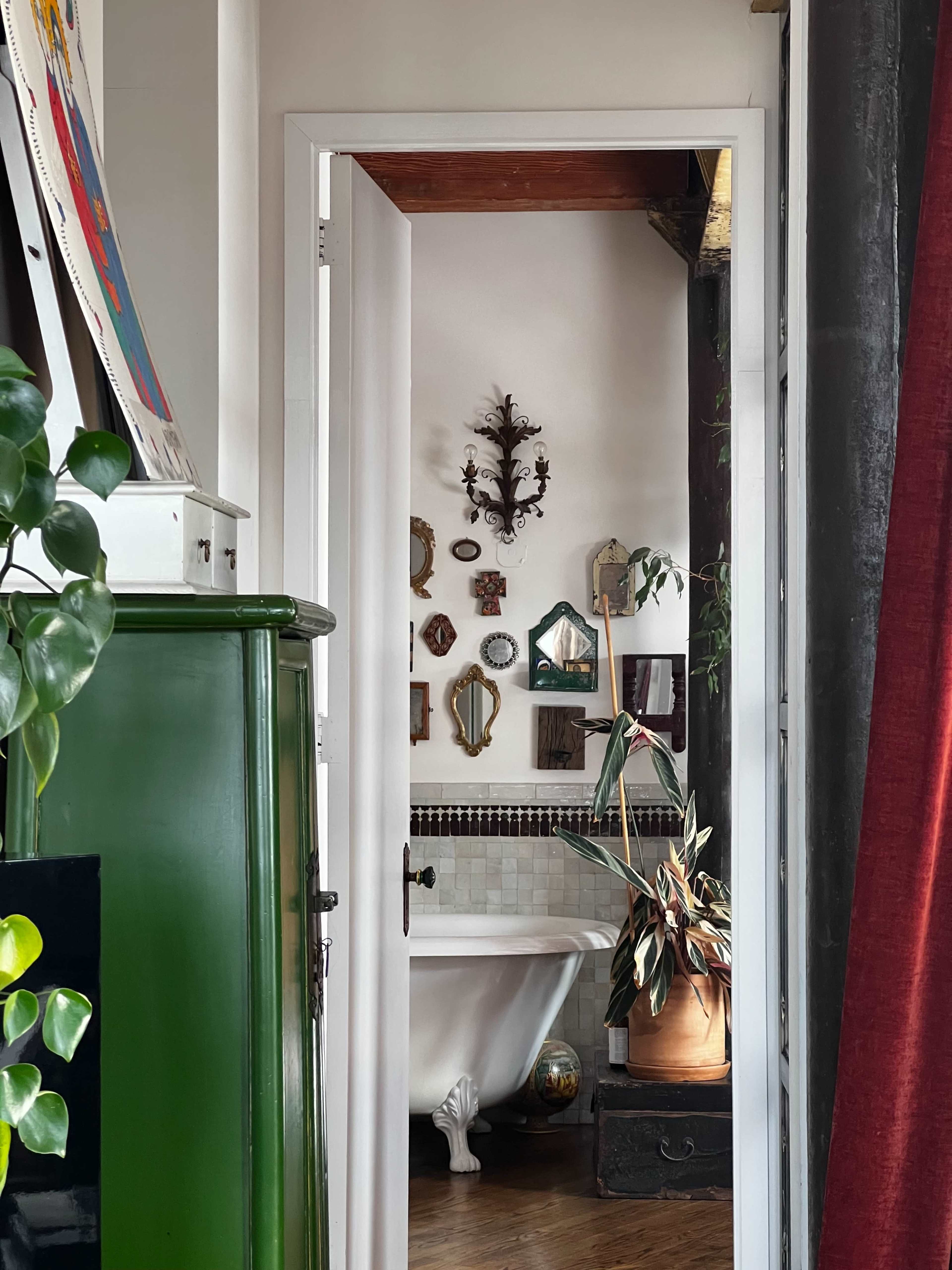A doorway frames a bathroom with a vintage bathtub and various decorative mirrors on the wall.